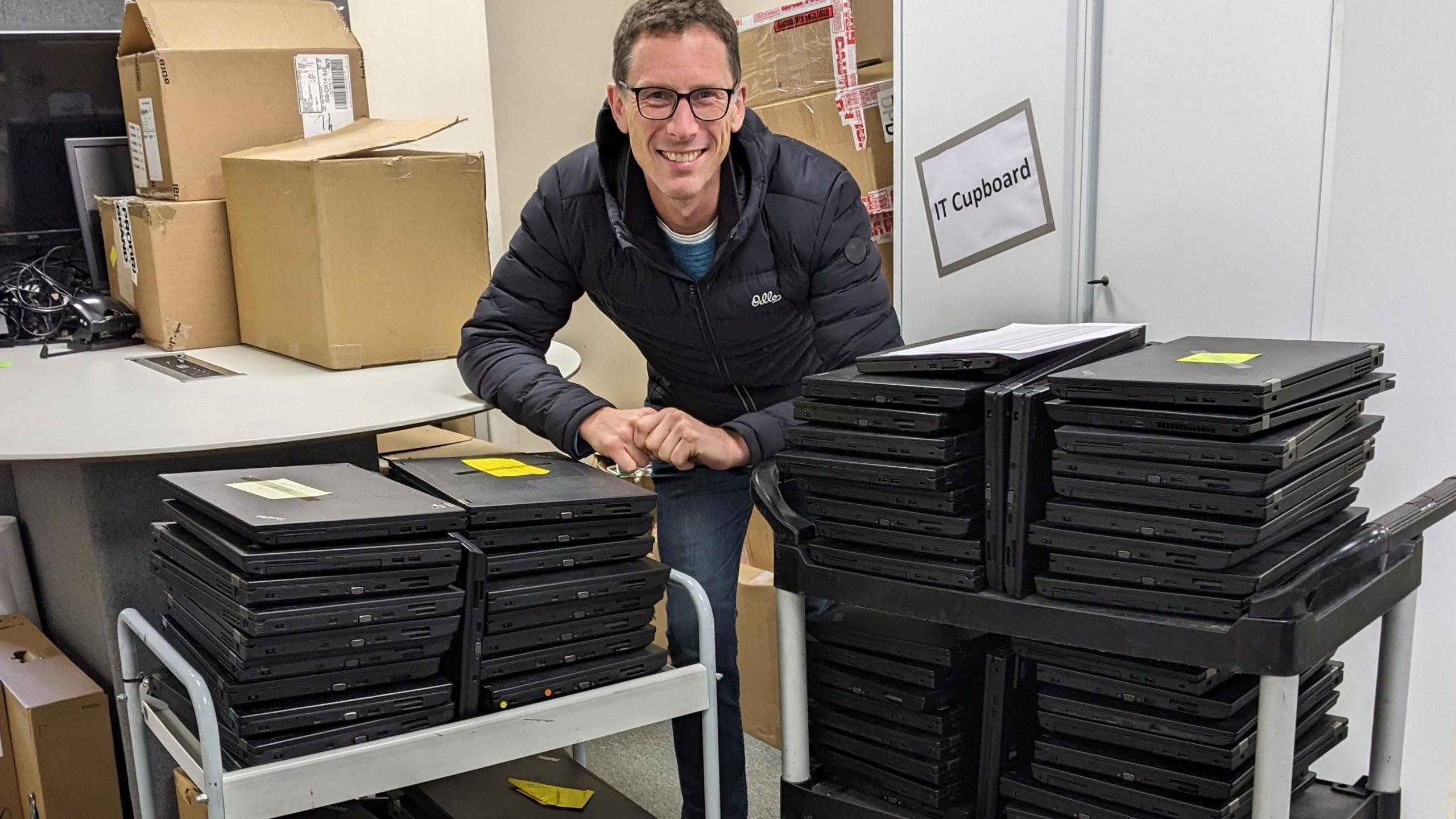 Ben Tuppen standing behind laptops in a blue jacket