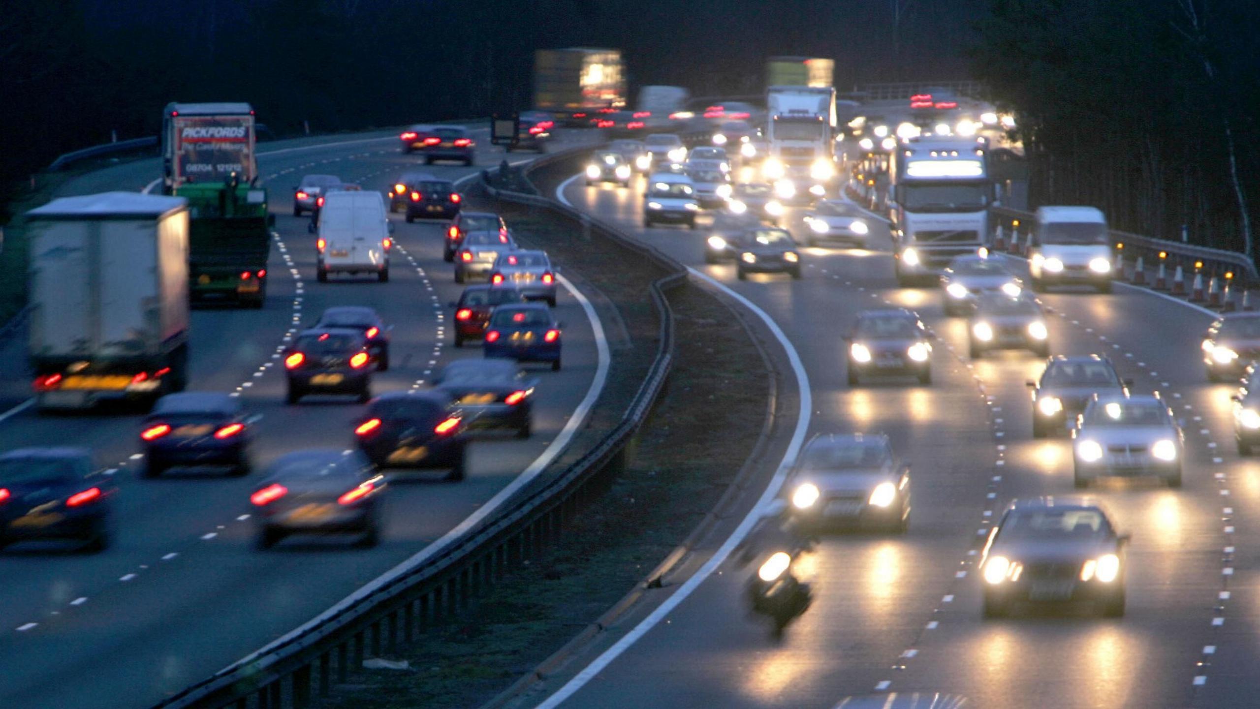 Cars driving along a busy motorway at night. There are three lanes of traffic travelling in each direction. You can see bright headlights and rear lights.