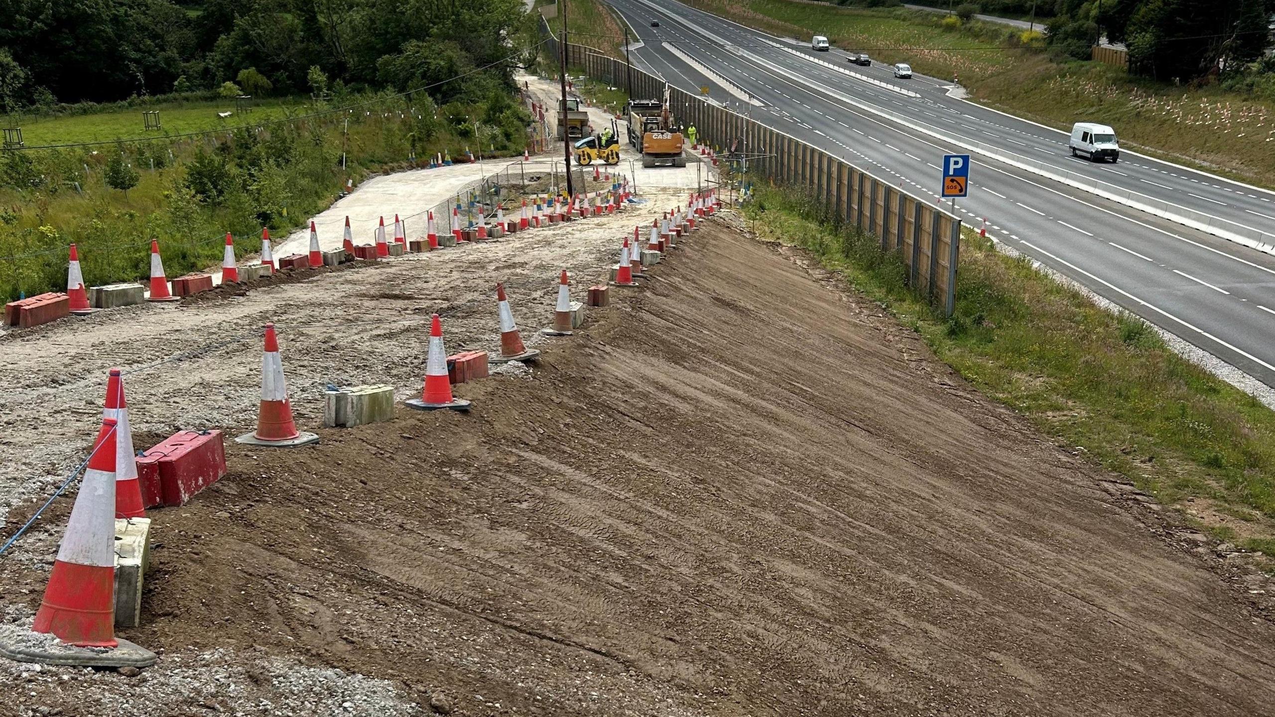 The side of the A30 which features a large bank of top soil and several traffic cones laid out in a line