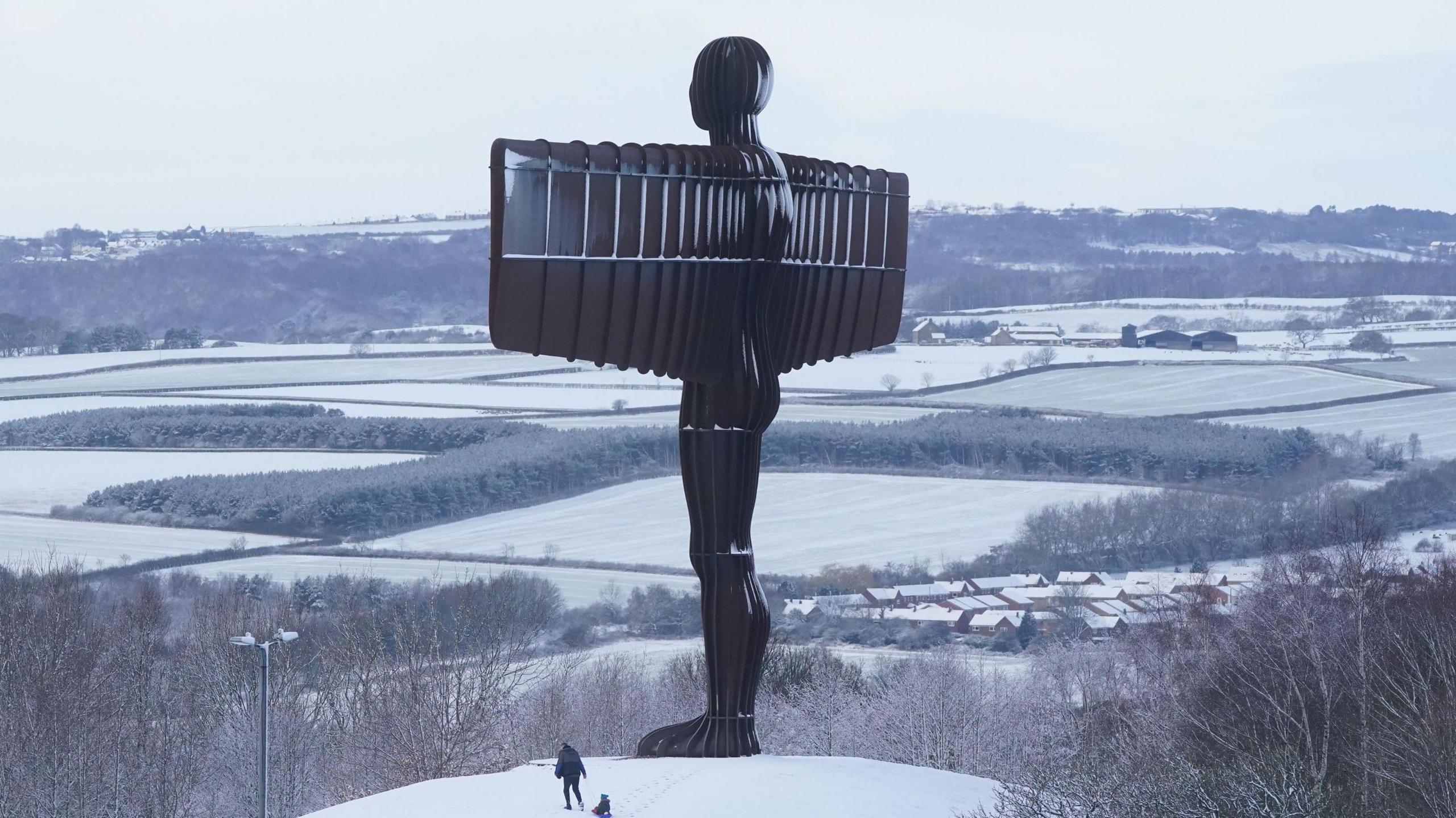 People sledging in the snow at the foot of Antony Gormley's Angel of the North sculpture in Gateshead. The tall sculpture, which resembles a man with rectangular wings, is dusted with snow.