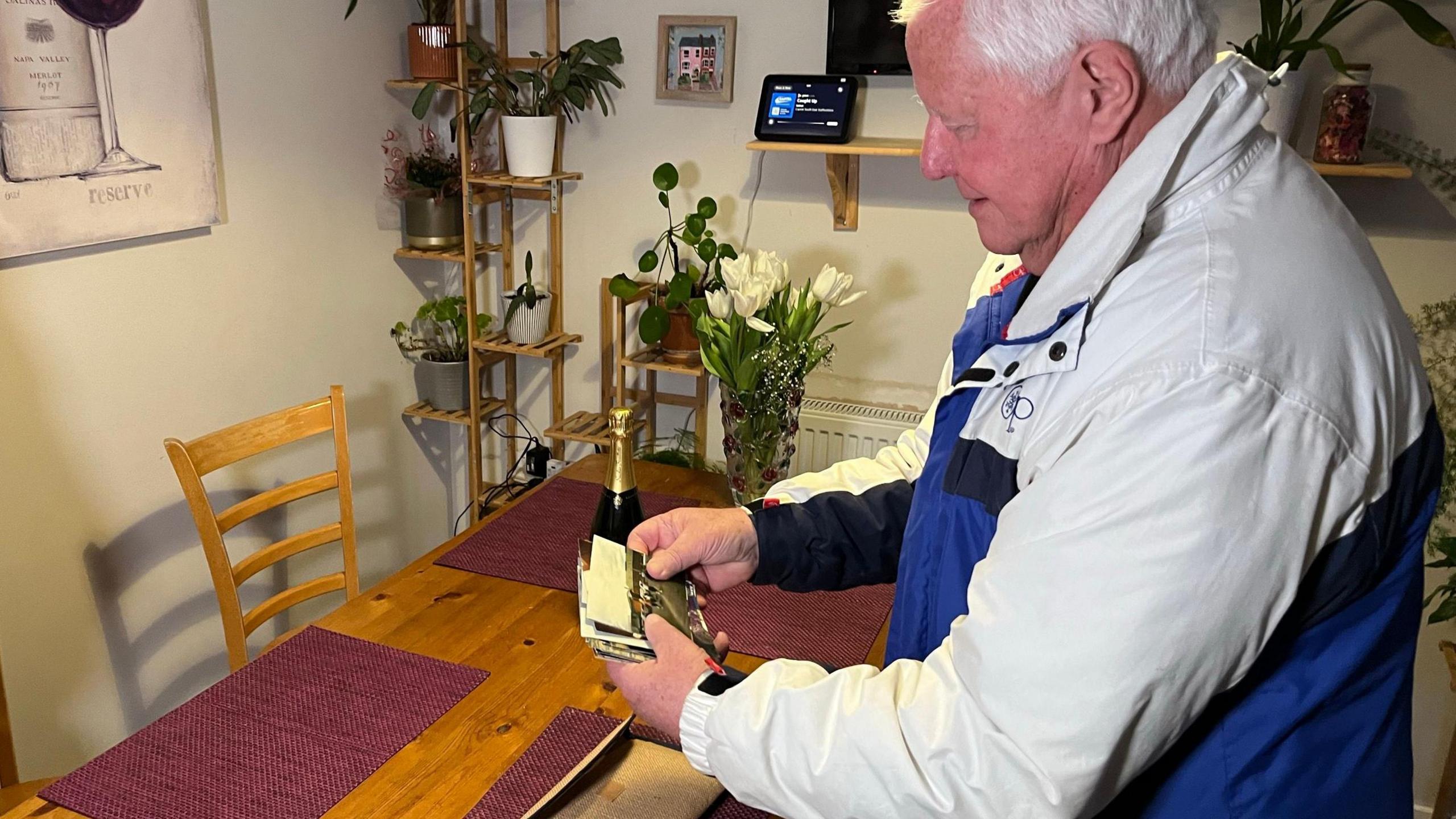 Tom Phillips looking at the photos - there is a bottle of champagne on the table.