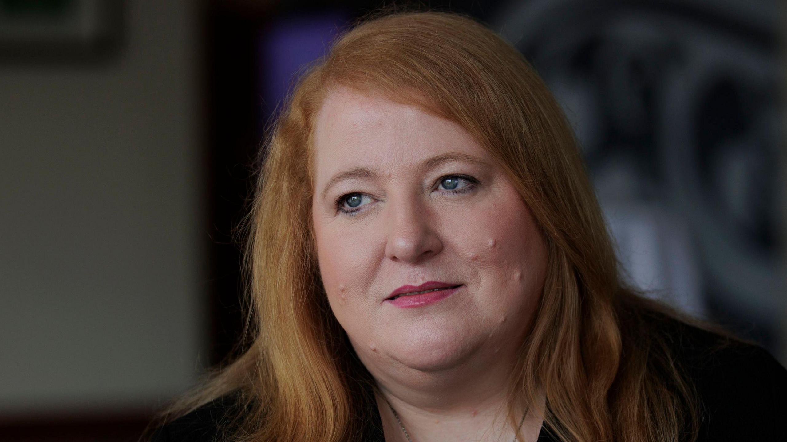 Naomi Long who has long light red hair and is wearing a black top and jacket.