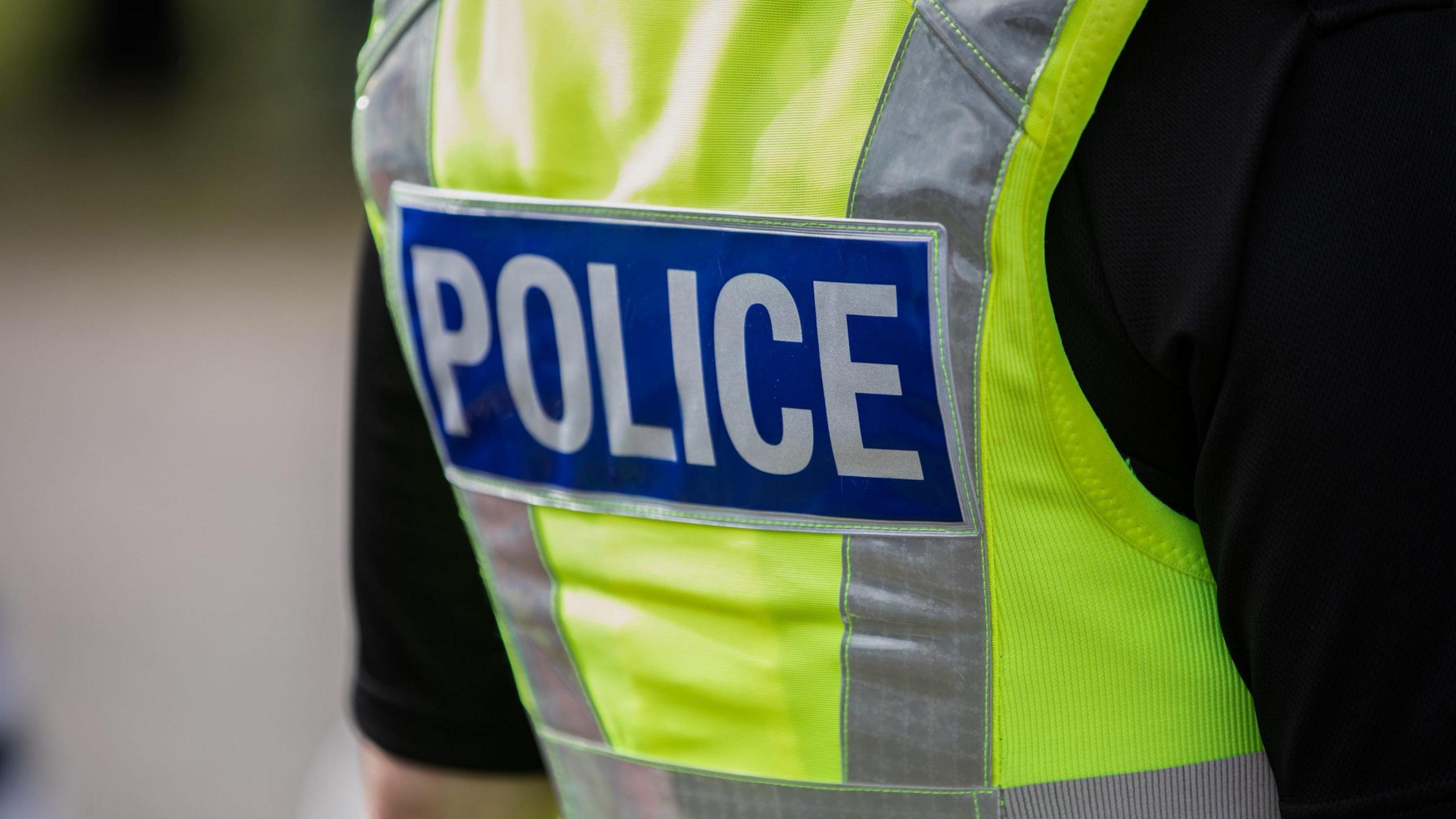 A police officer pictured from behind, showing just their torso. They are wearing a black t-shirt and high-vis top.