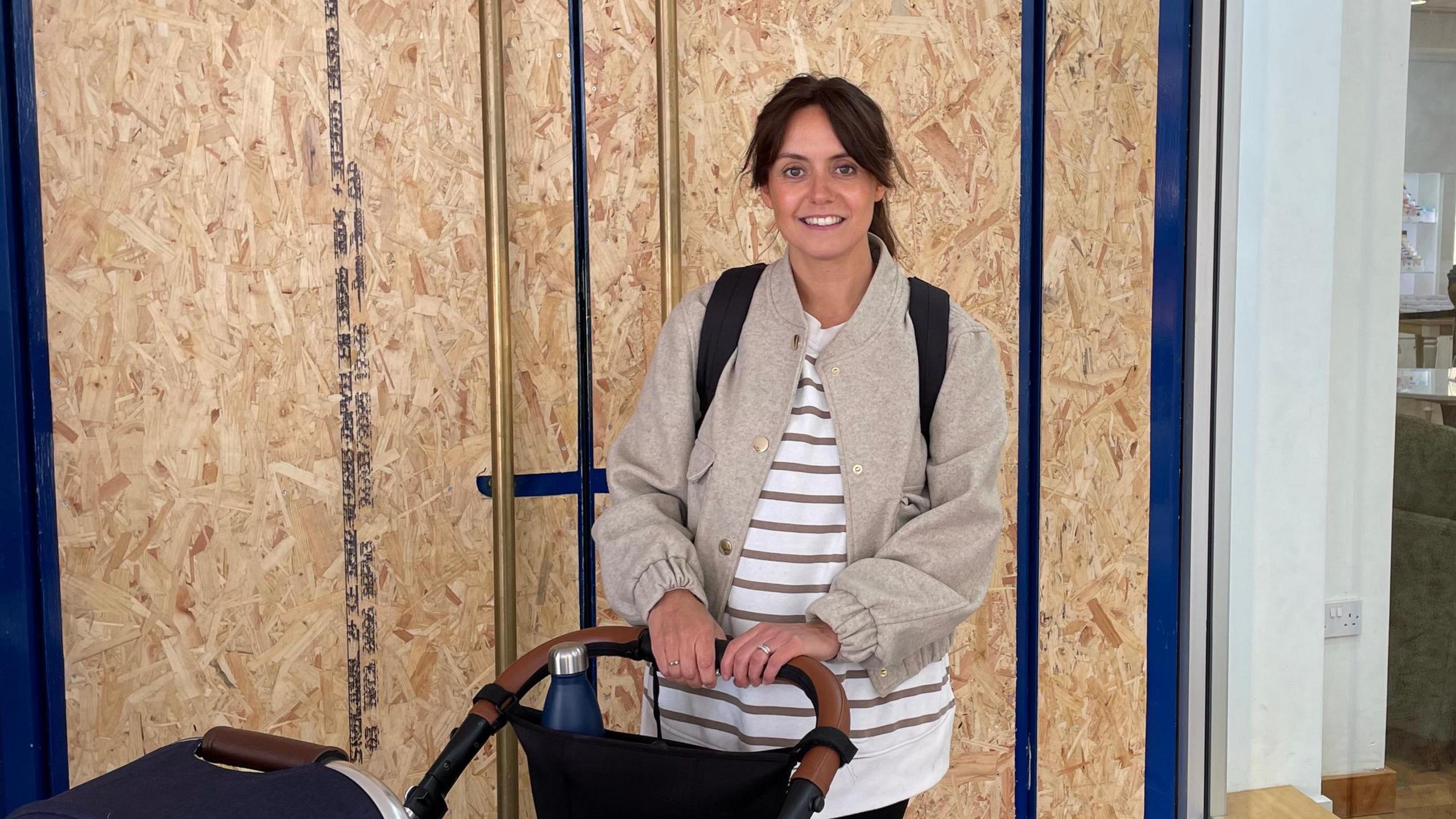 Rebecca Turner stands in front of doors with boards on with a pram