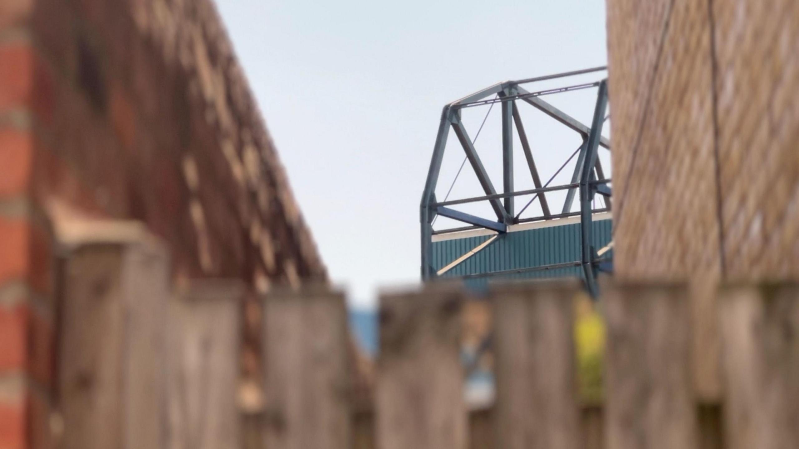 Sheffield Wednesday's North Stand seen through the gates of a terraced house. The Stand is blue - and in focus while the gate and houses are defocussed.