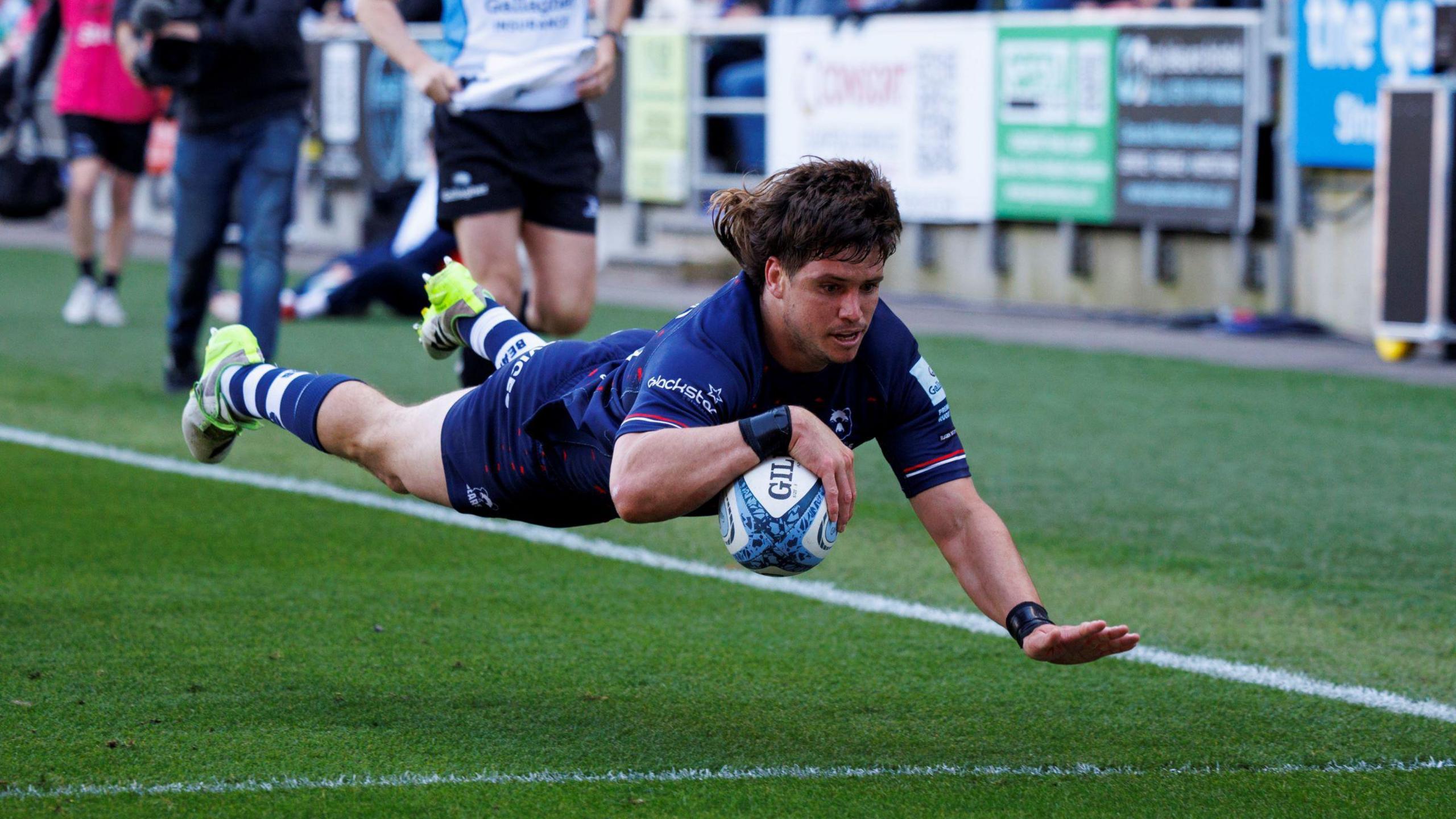 Bristol Bears' Benhard Janse van Rensburg scores a try during the Gallagher Premiership Rugby match between Bristol Bears and Newcastle Falcons at Ashton Gate. He is pictured airborne as he approaches the try line with the ball in his right hand and his left hand poised to control his landing.