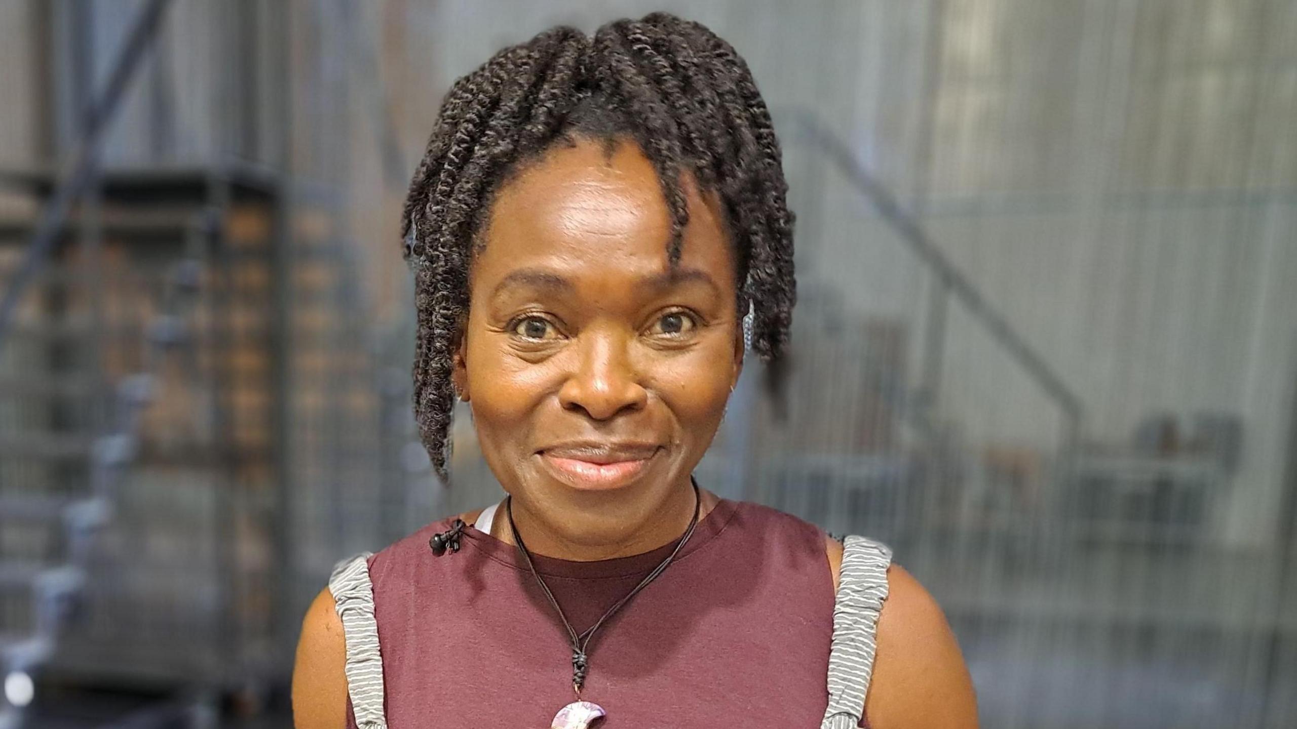 Mae Rakie Ayola n gwenu ar y camera. Mae ganddi wallt tywyll a mae'n gwisgo mwclus sy'n edrych fel lleuad gyda chris coch.