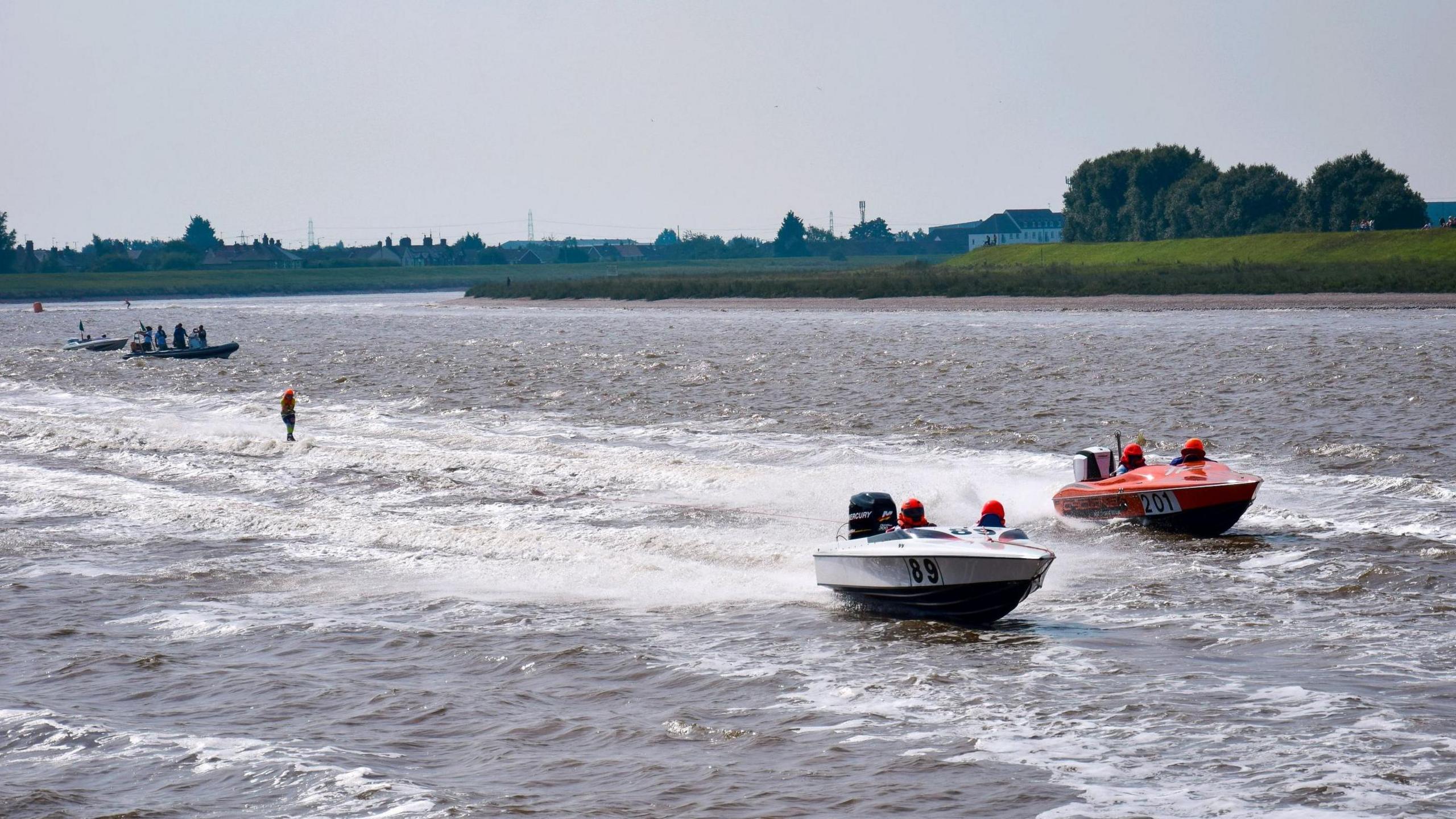 Boats racing along the Great Ouse river. In the background, there are the green banks of the river.