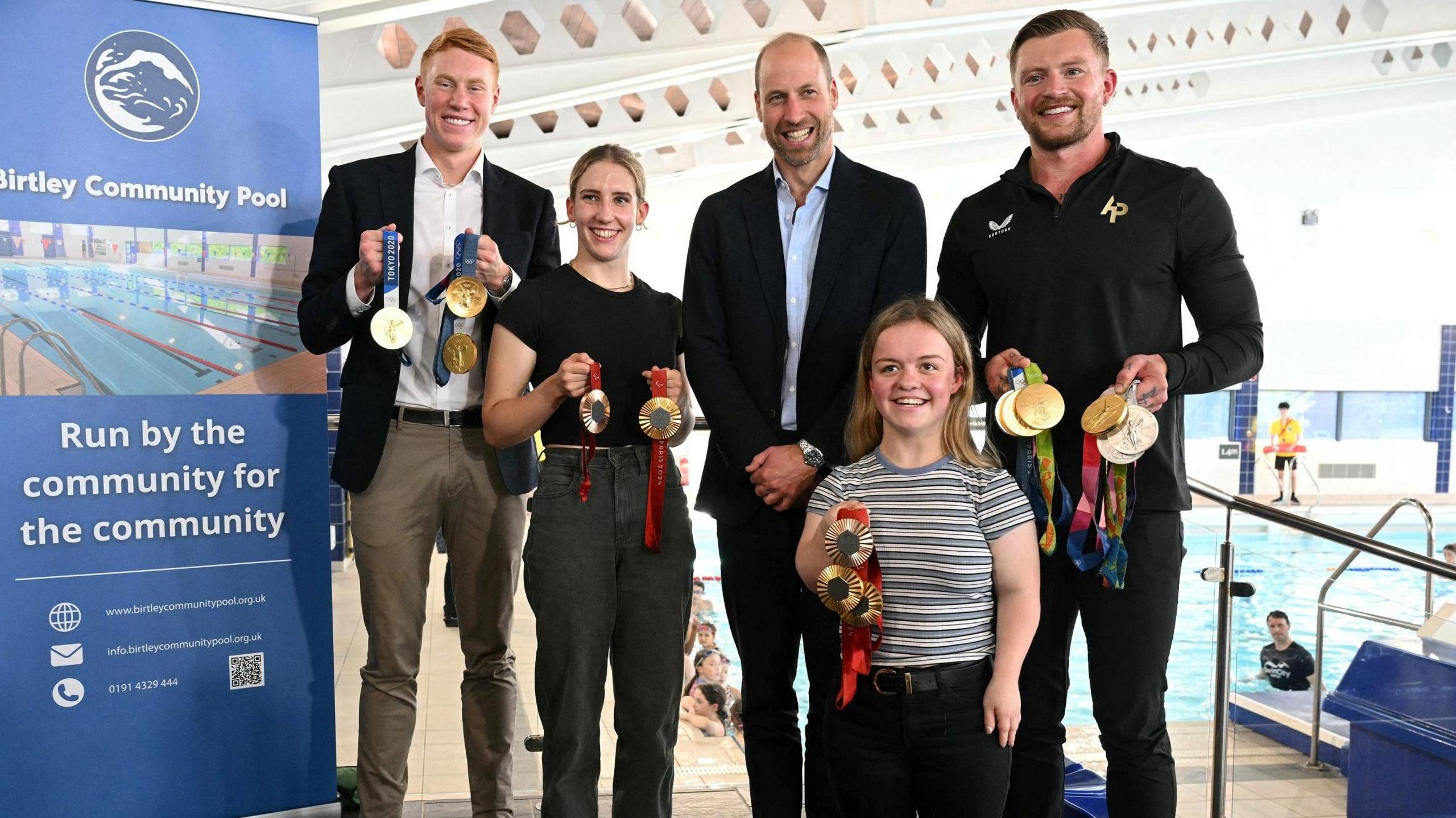 Prince William poses in the middle of British Olympians and Paralympians Adam Peaty, Tom Dean, Maisie Summers-Newton and Louise Fiddes, by the side of the swimming pool.