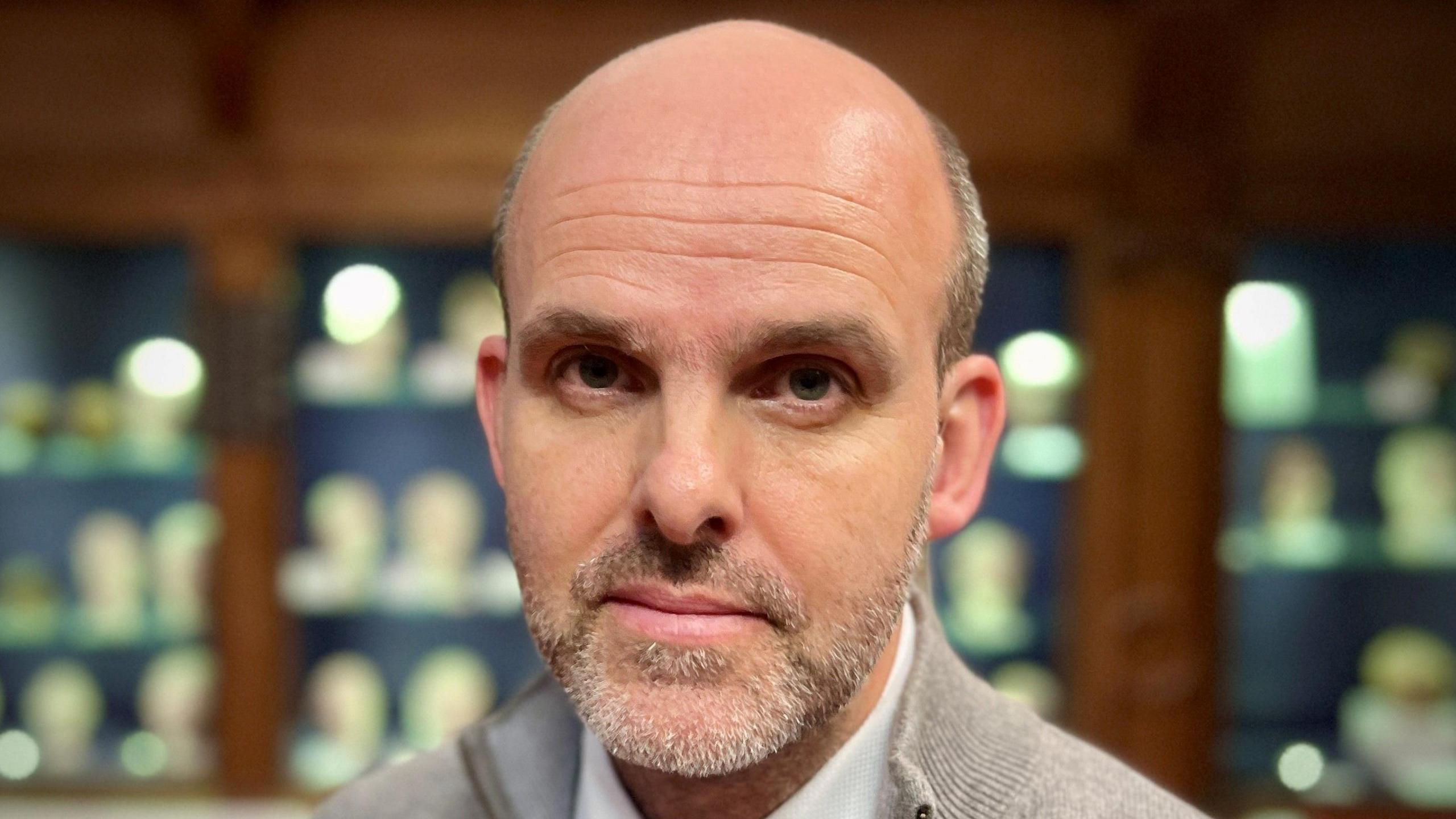 Prof Tom Gillingwater looking directly at the camera, standing in front of a display case