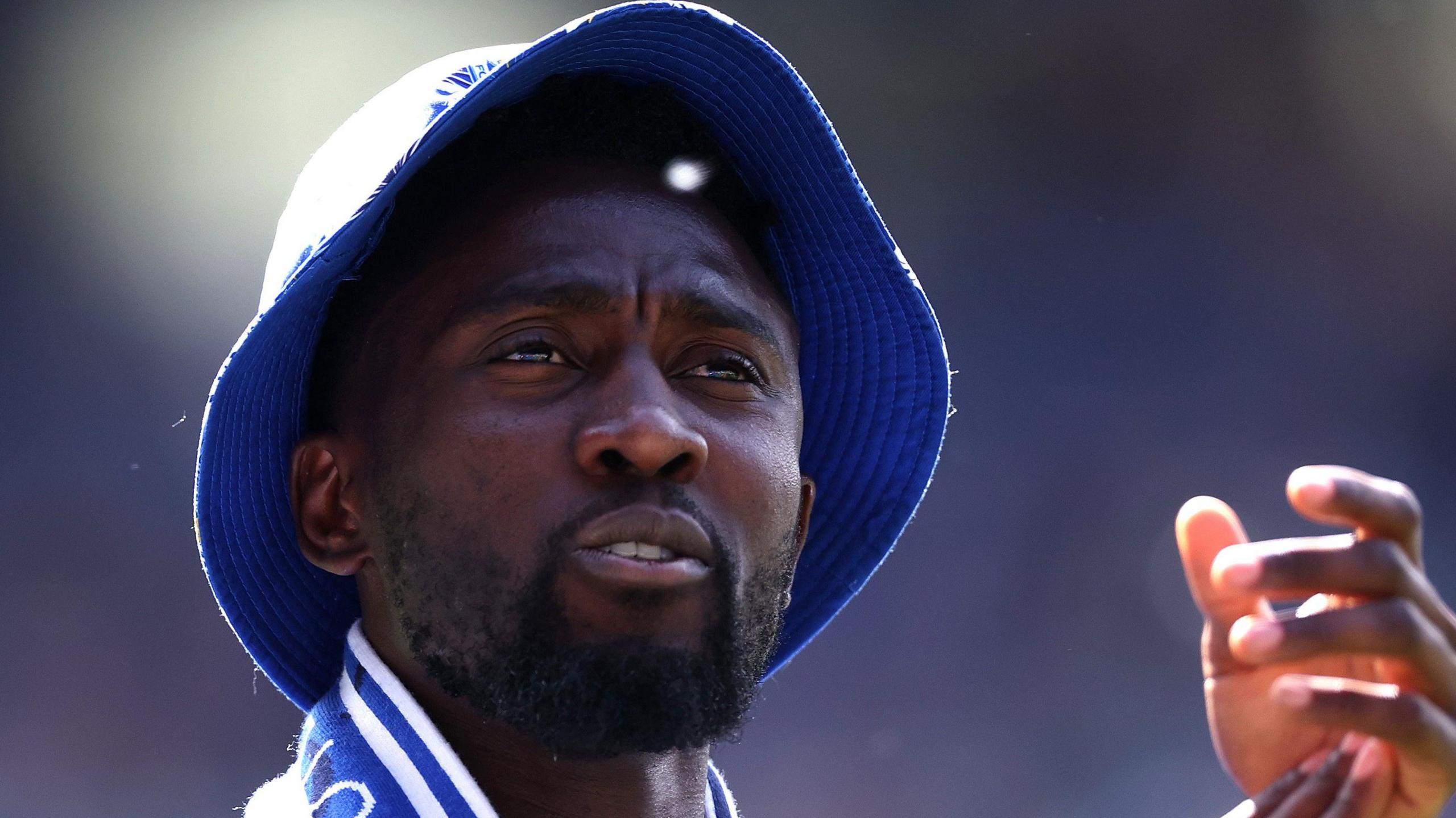 A close up of Wilfred Ndidi wearing a blue hat and clapping fans