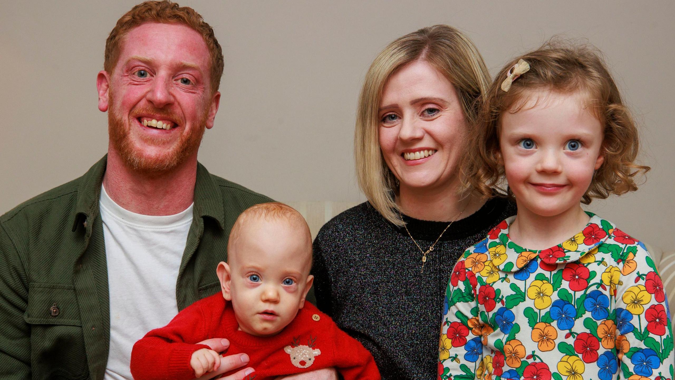 Lindsay Ace, Matthew Ace, four-year-old Aine Ace and Iarla Ace all smile at the camera. Iarla is on his father's knee.