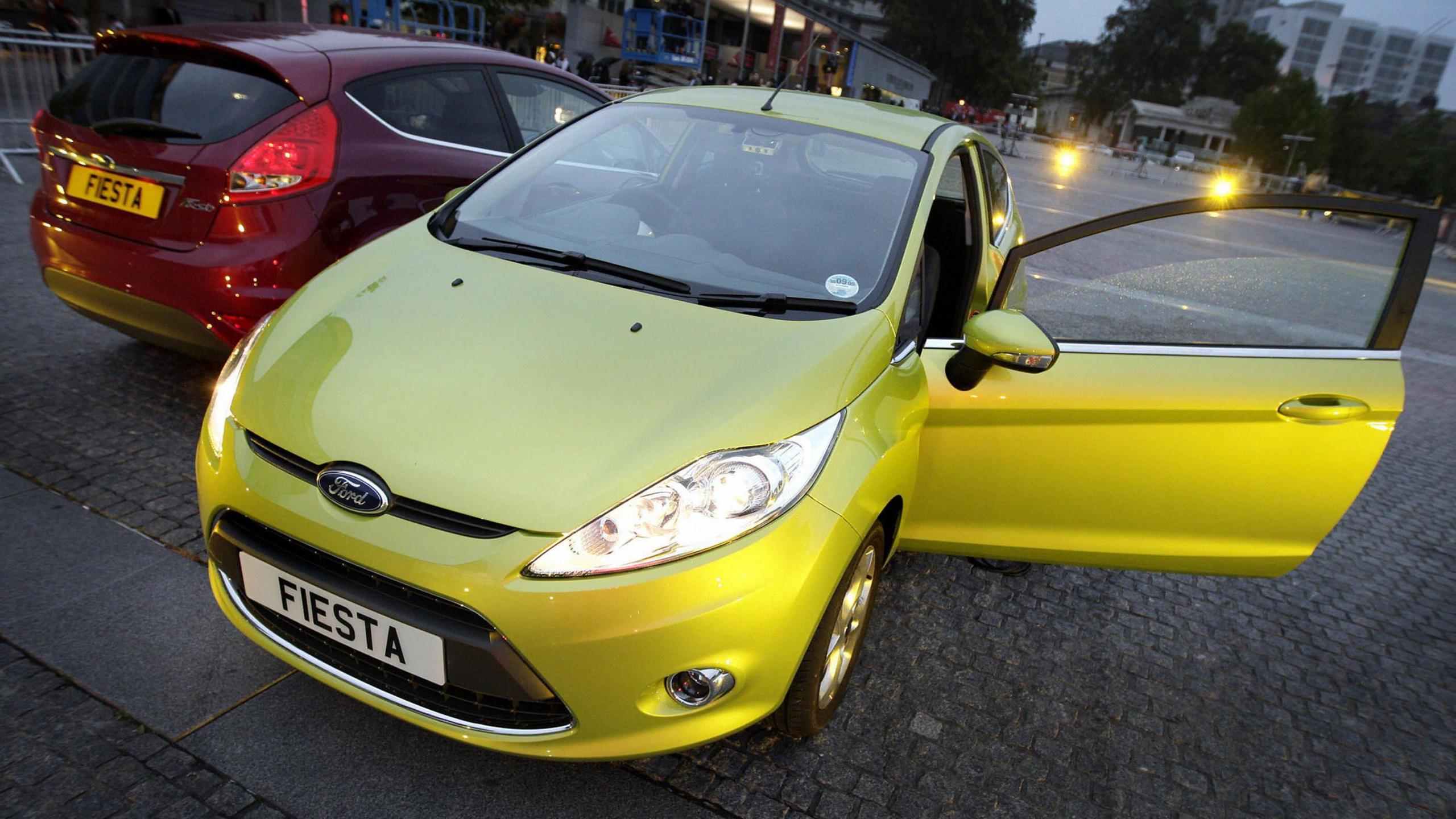 Two ford fiestas are parked side by side. One is red and one is yellow.