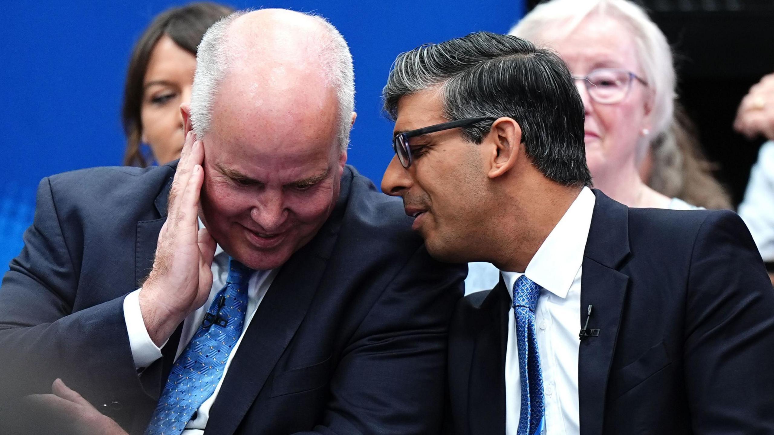 Andrew RT Davies at with Rishi Sunak in front of a blue background. Both are wearing dark blue suits and with light blue ties.