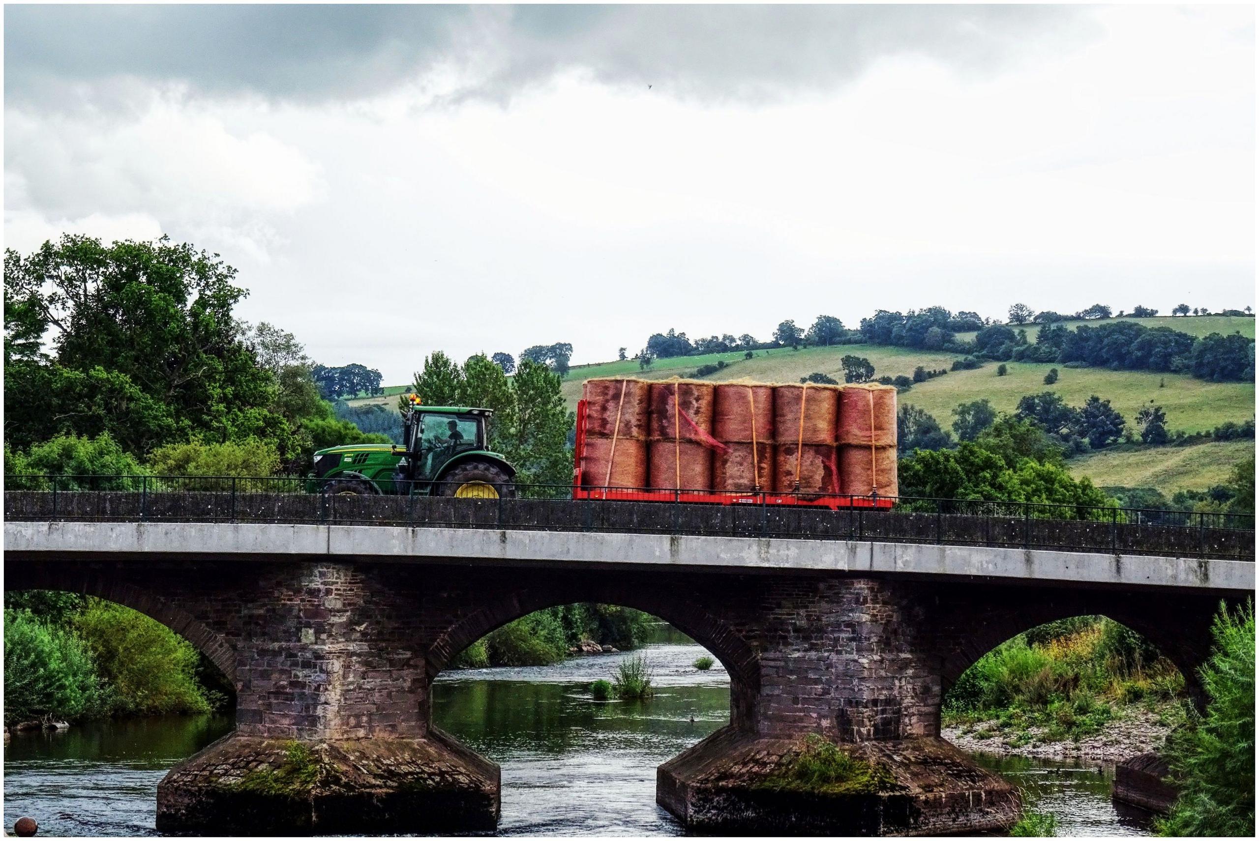 A tractor pulls a trailer of hay across a bridge