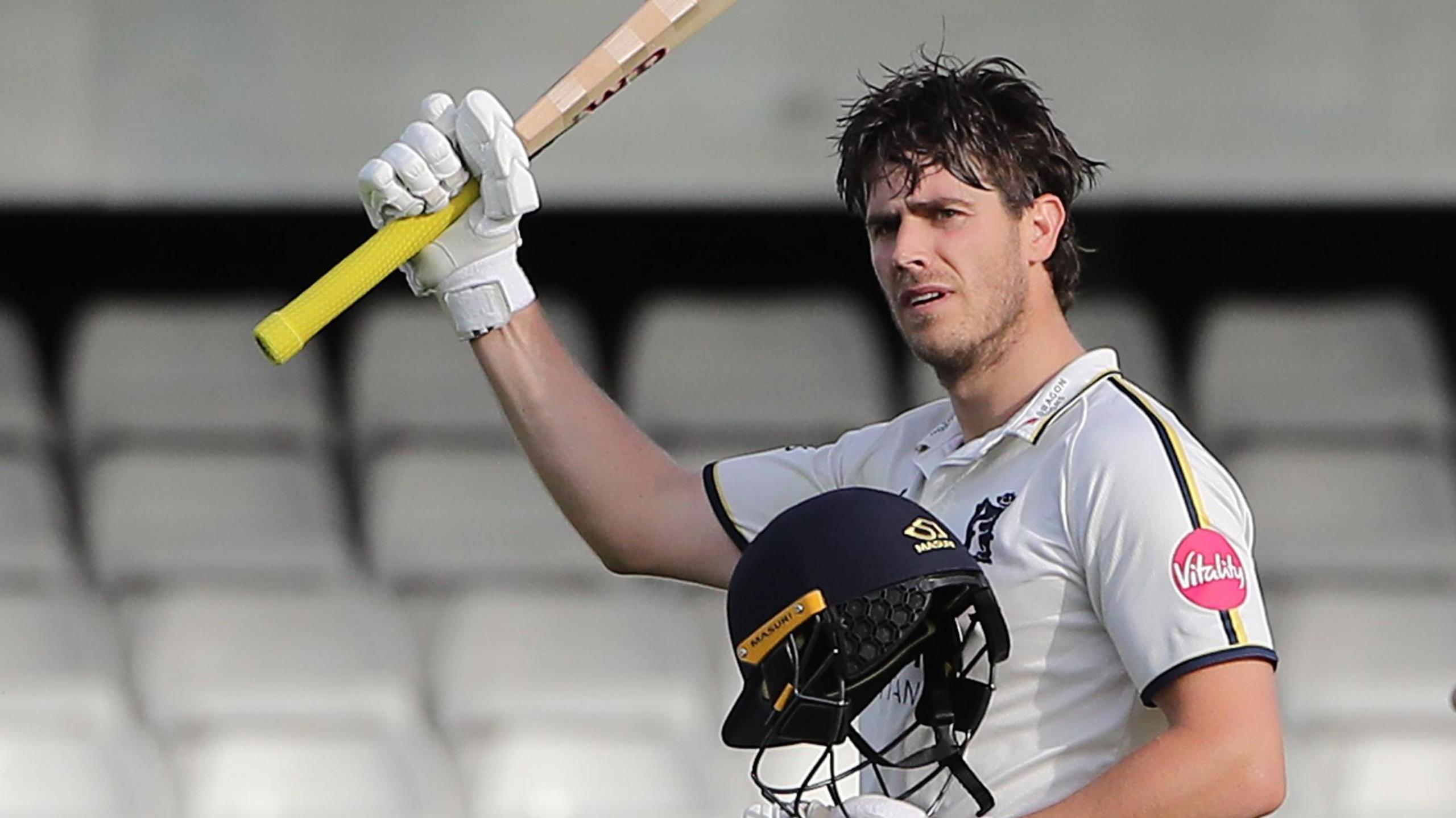 Michael Burgess holds his bat aloft after reaching a century for Warwickshire