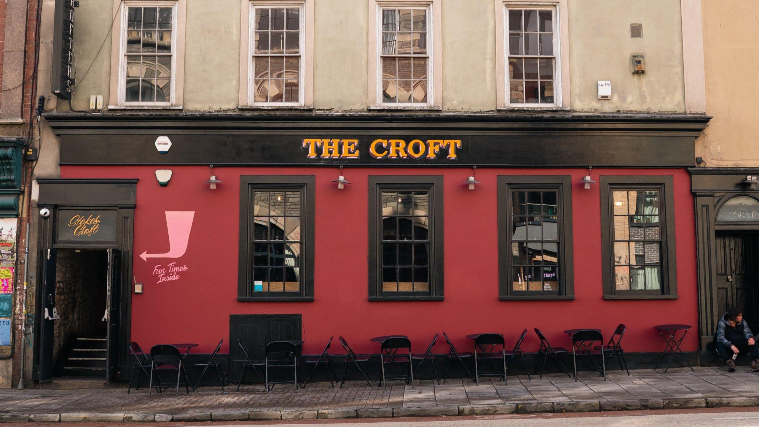 The red-walled exterior of The Croft, which looks like a pub from the outside. A black door is open with black steps leading upwards.