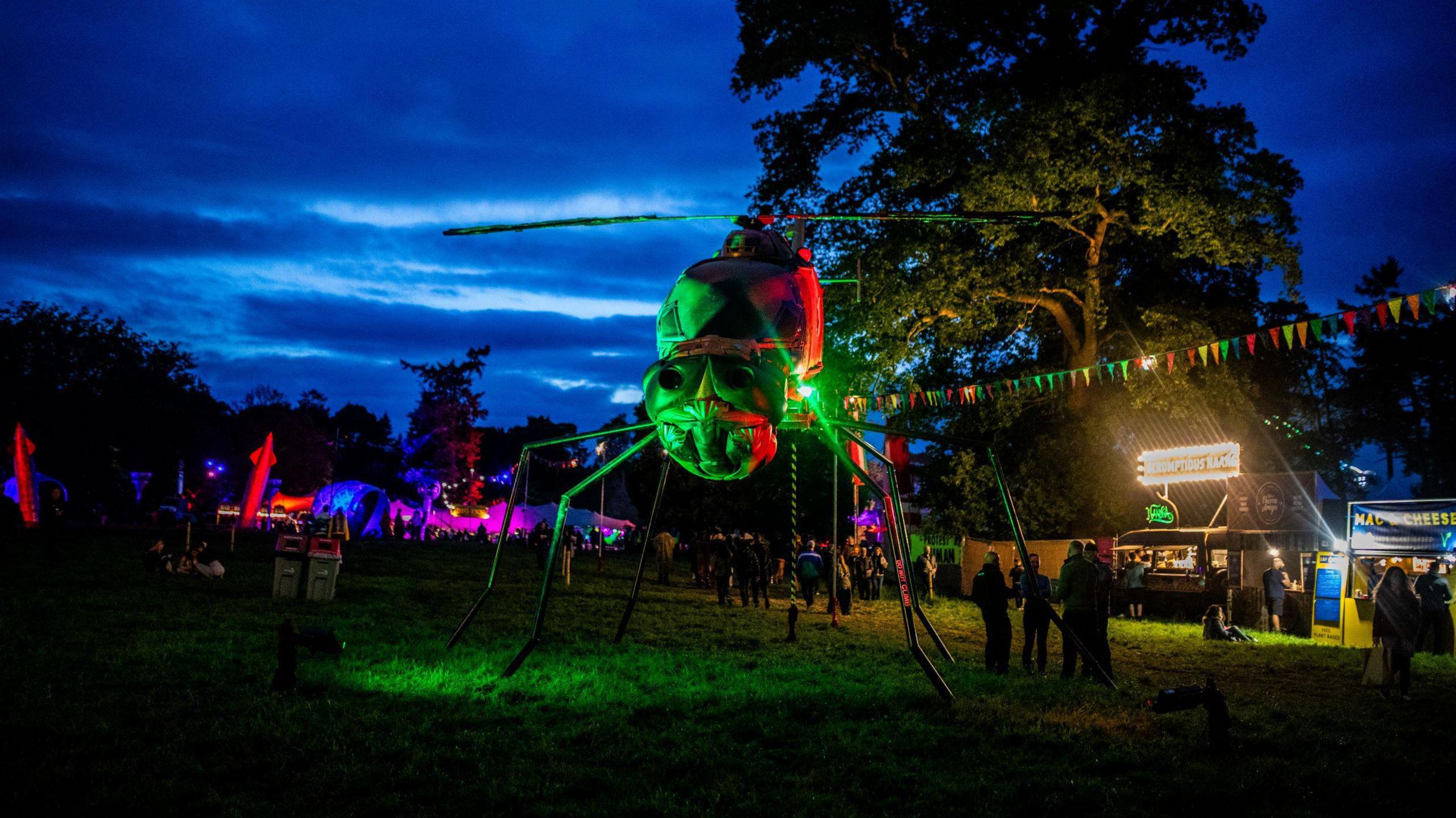 A large spider structure near some food vans at a festival