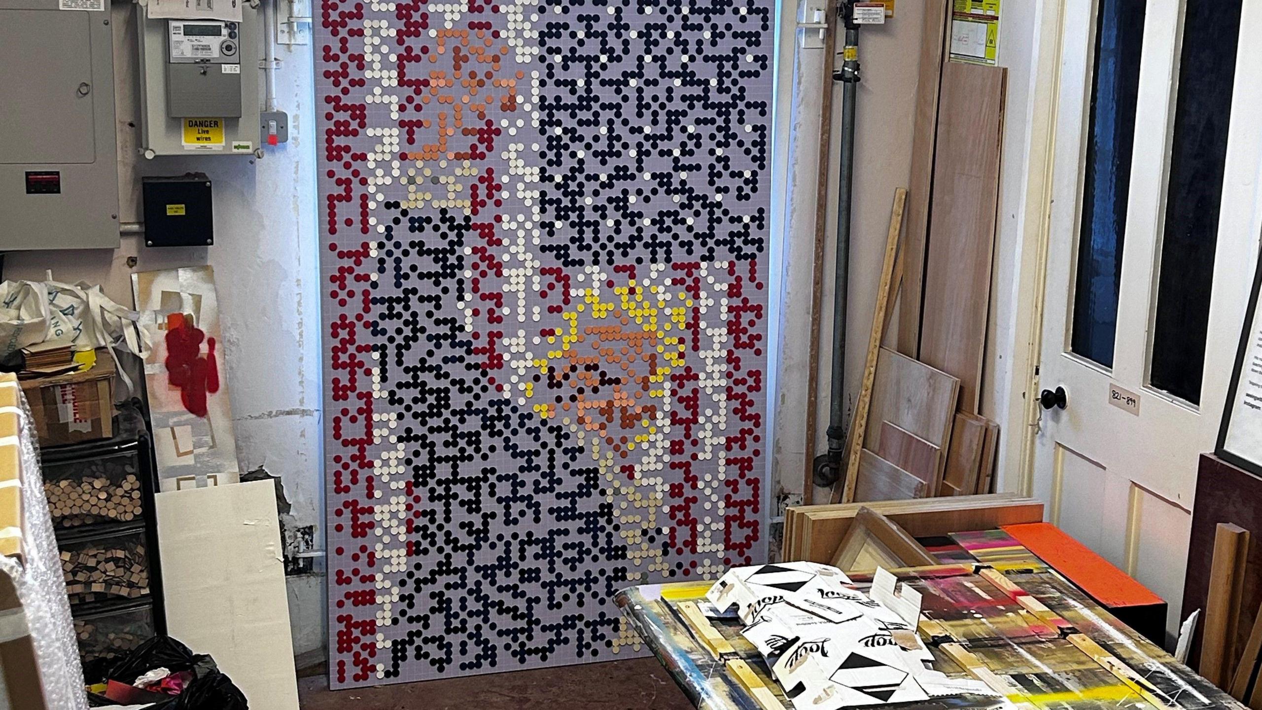 A board mounted in an art studio has coloured dots. The pixillated image shows a blond Donald Trump in a dark suit with his arm aloft in front of a US flag.