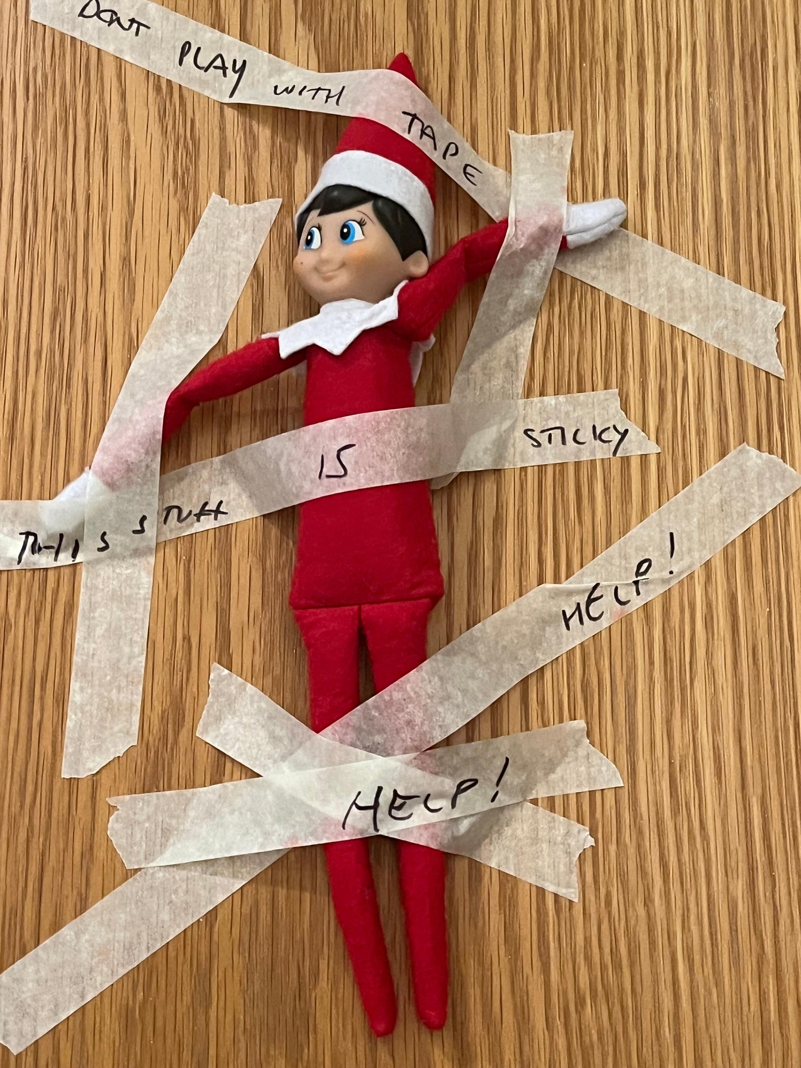 A elf is stuck to a door with tape with words written on it.