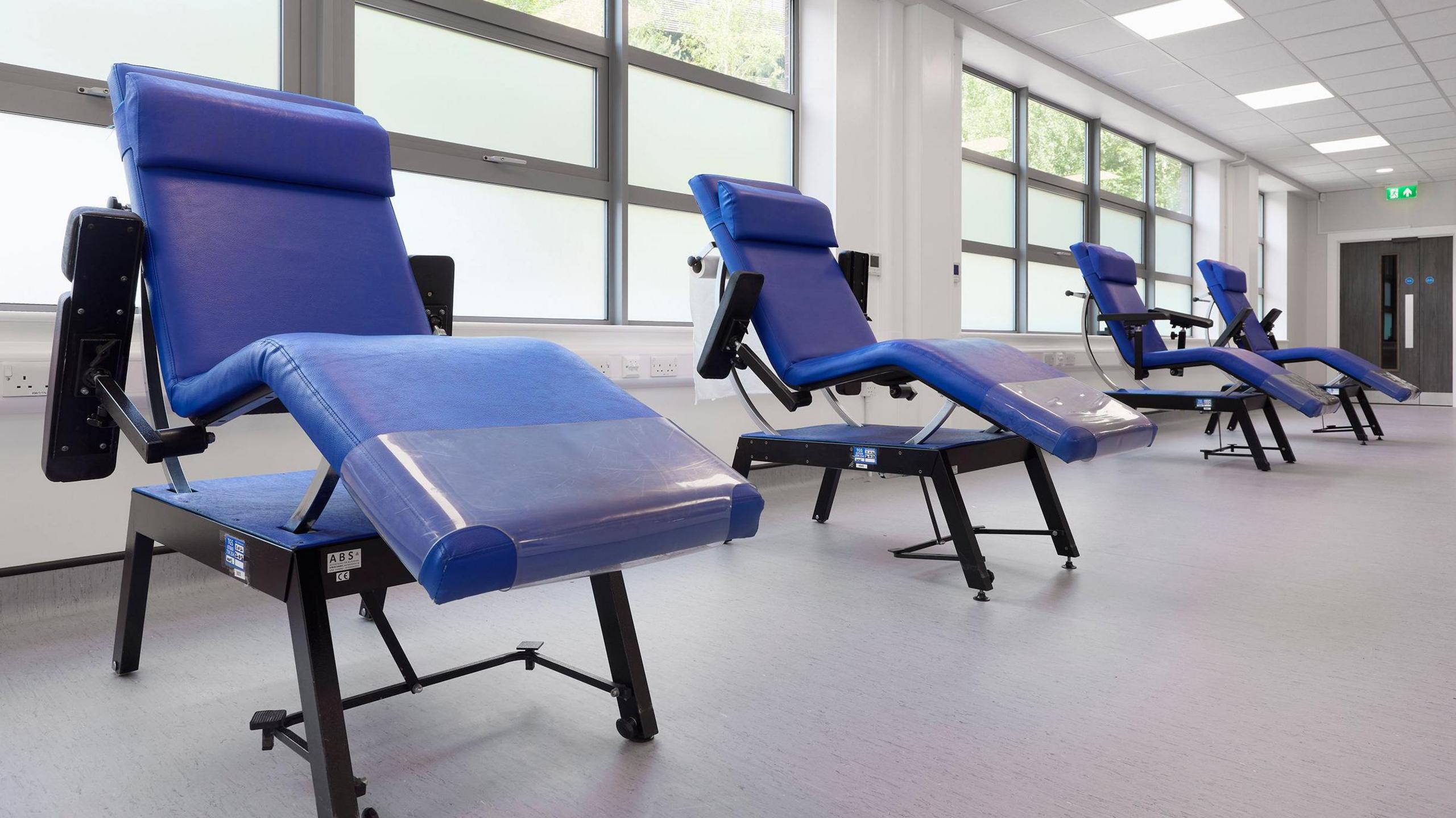 Four blue blood donor chairs in a large room.