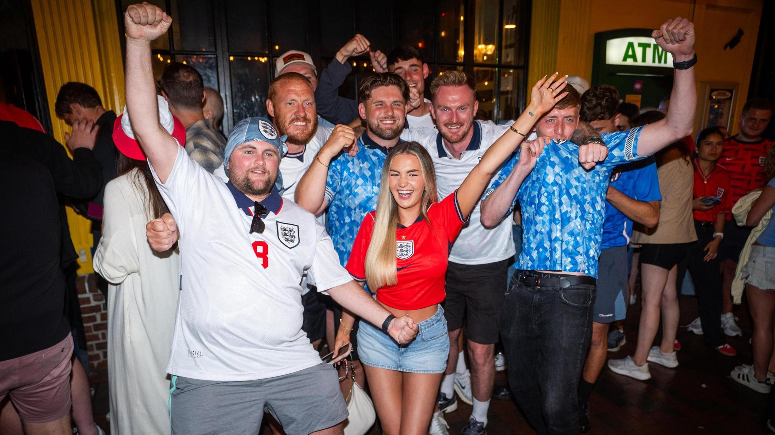 England fans, wearing assorted coloured shirts, pose outside a bar in Boston