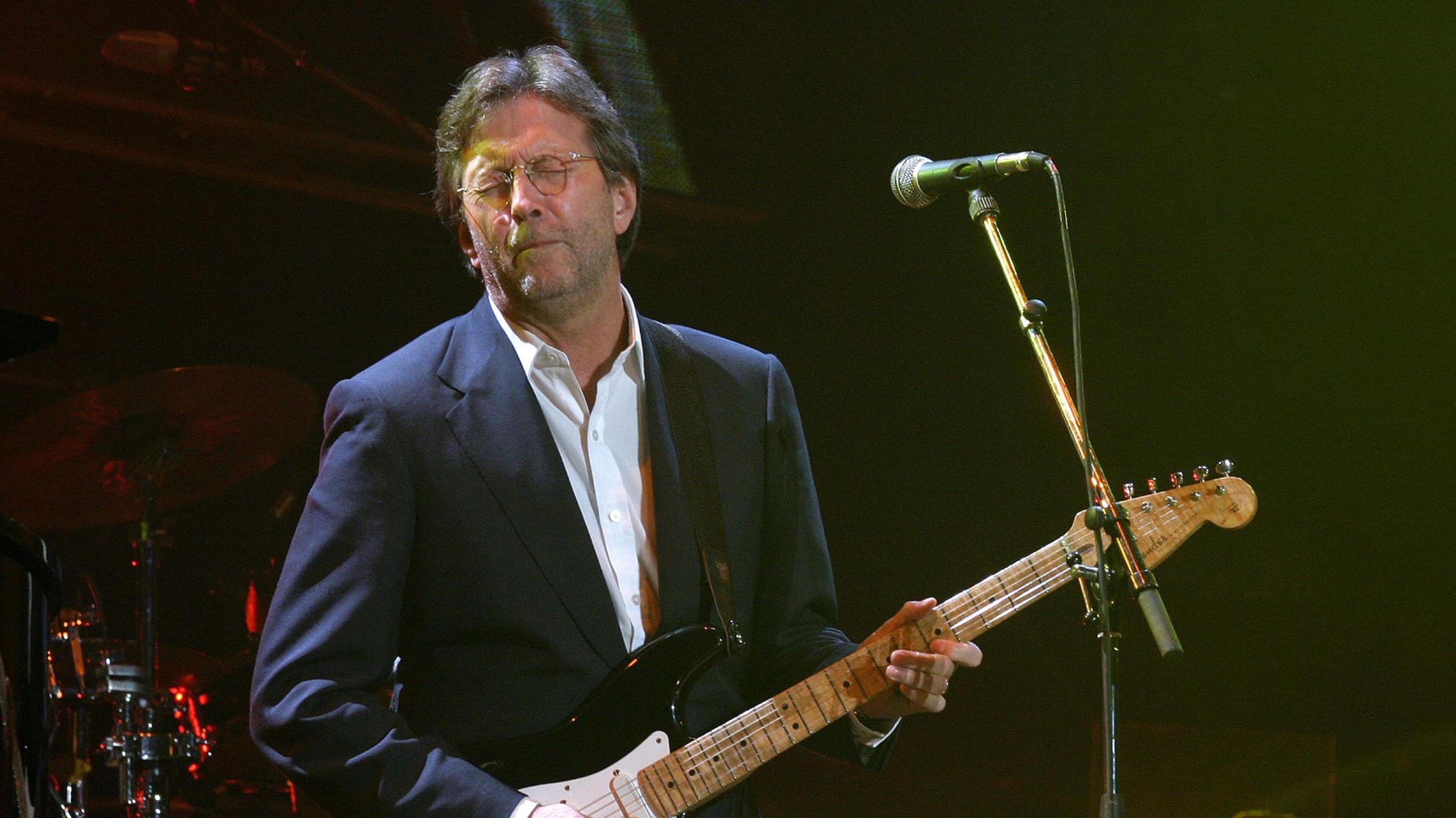 Eric Clapton, wearing a suit and with eyes closed, plays his electric guitar at Tsunami Relief Cardiff