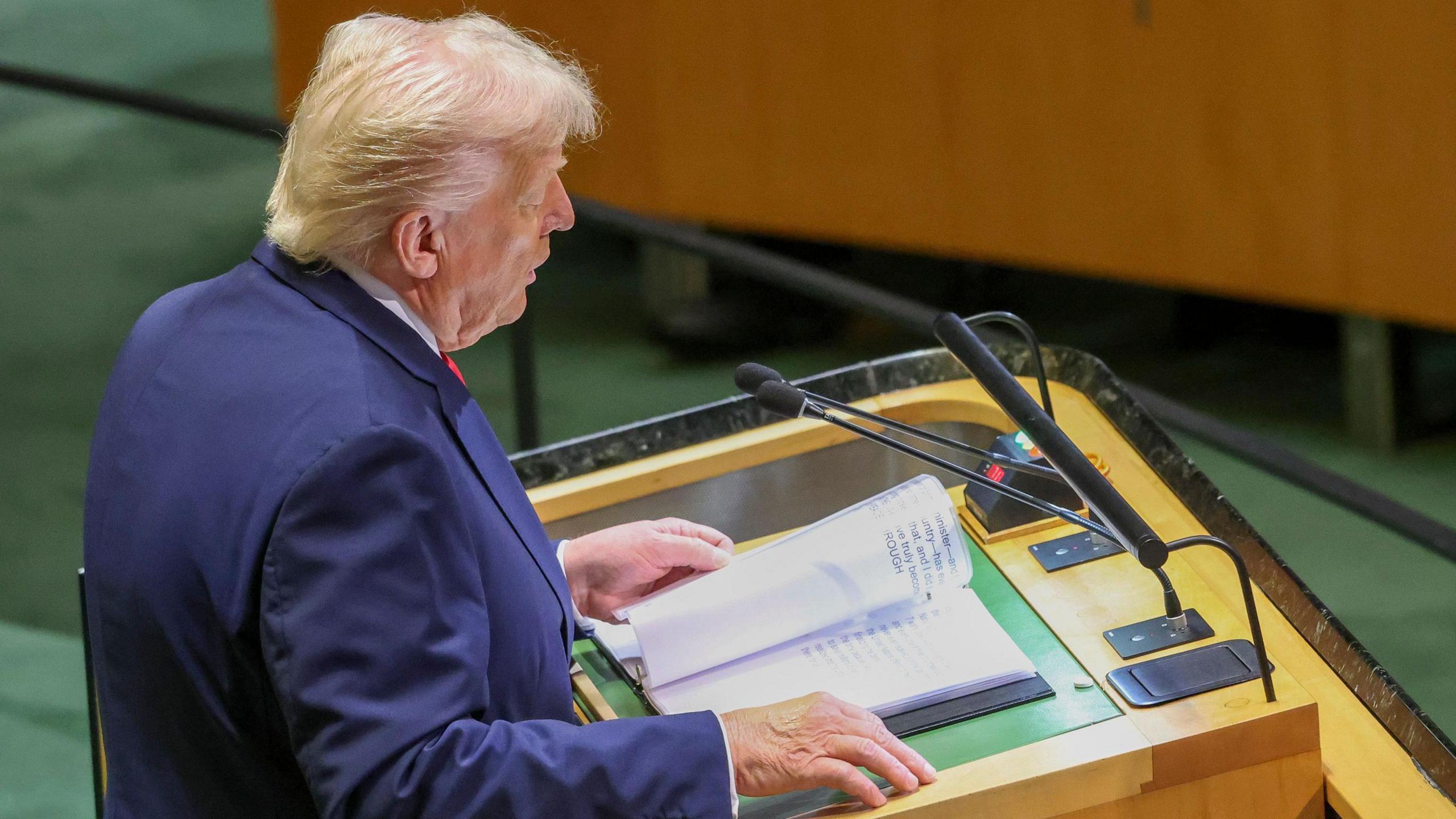 A photo of Donald Trump as he speaks to the UN General Assembly from a podium. The angle of the picture captures a photo of his binder with his speech notes in a large font.