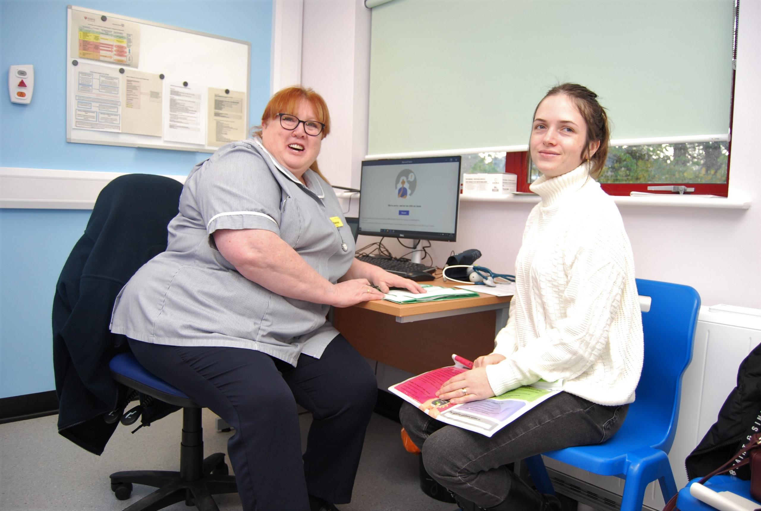 A midwife sits at a desk with a young woman wearing a white top