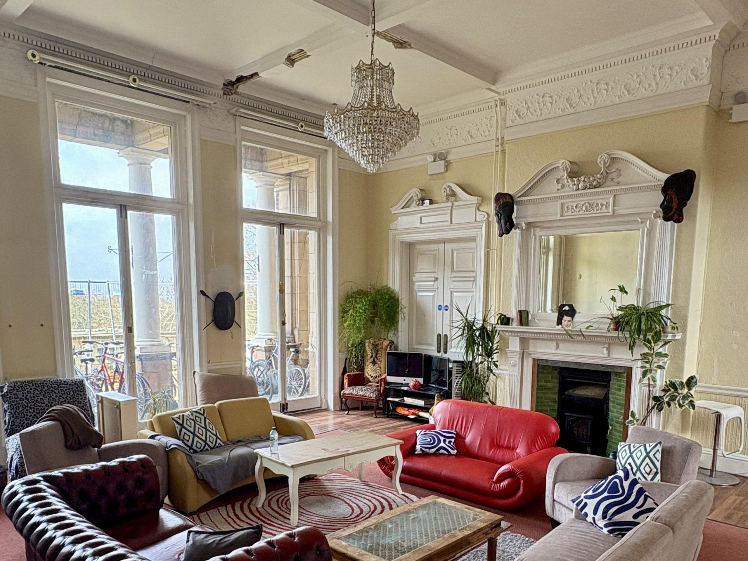 A large living room painted white with a chandelier hanging from the ceiling, a fireplace. 