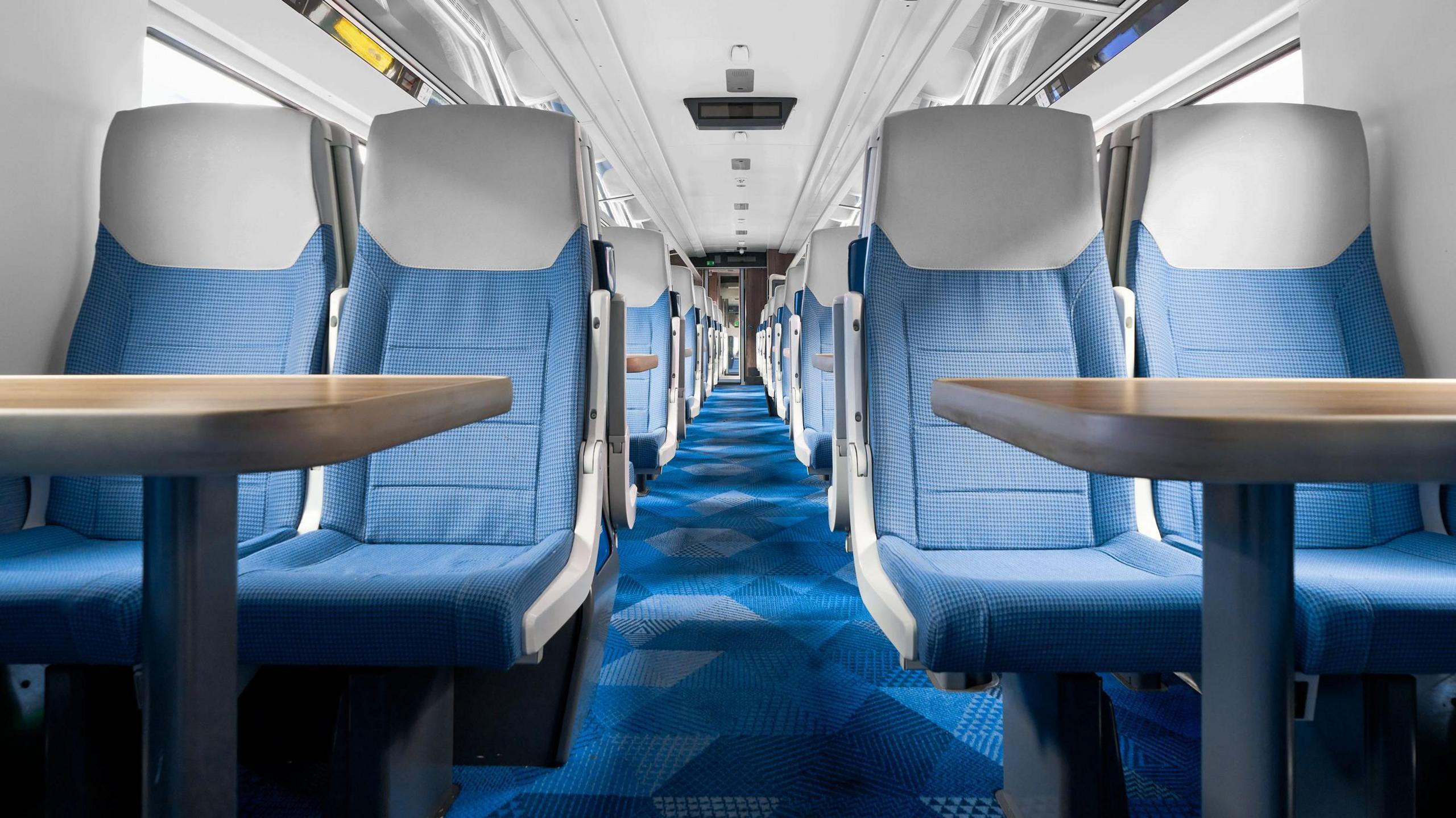 The interior of a Mark 5A train - it has blue seats and blue, geometrically patterned carpet.
