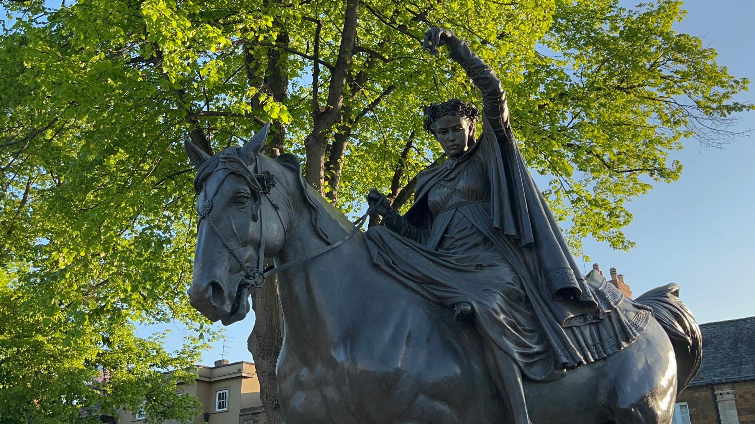 A shot of the statue against a sunny sky and a tree.
