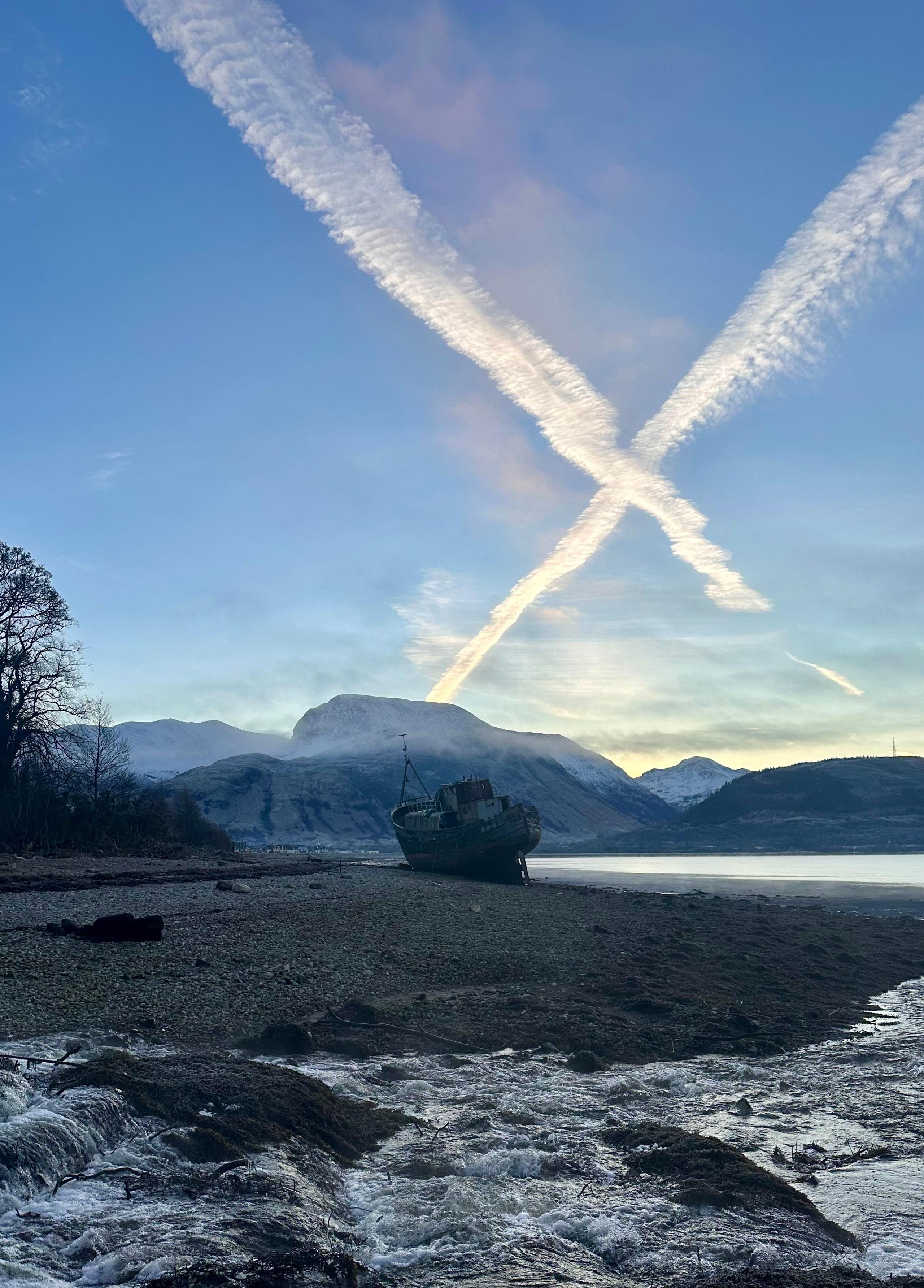 A mountain with a snowy foreground and a white cross in the sky