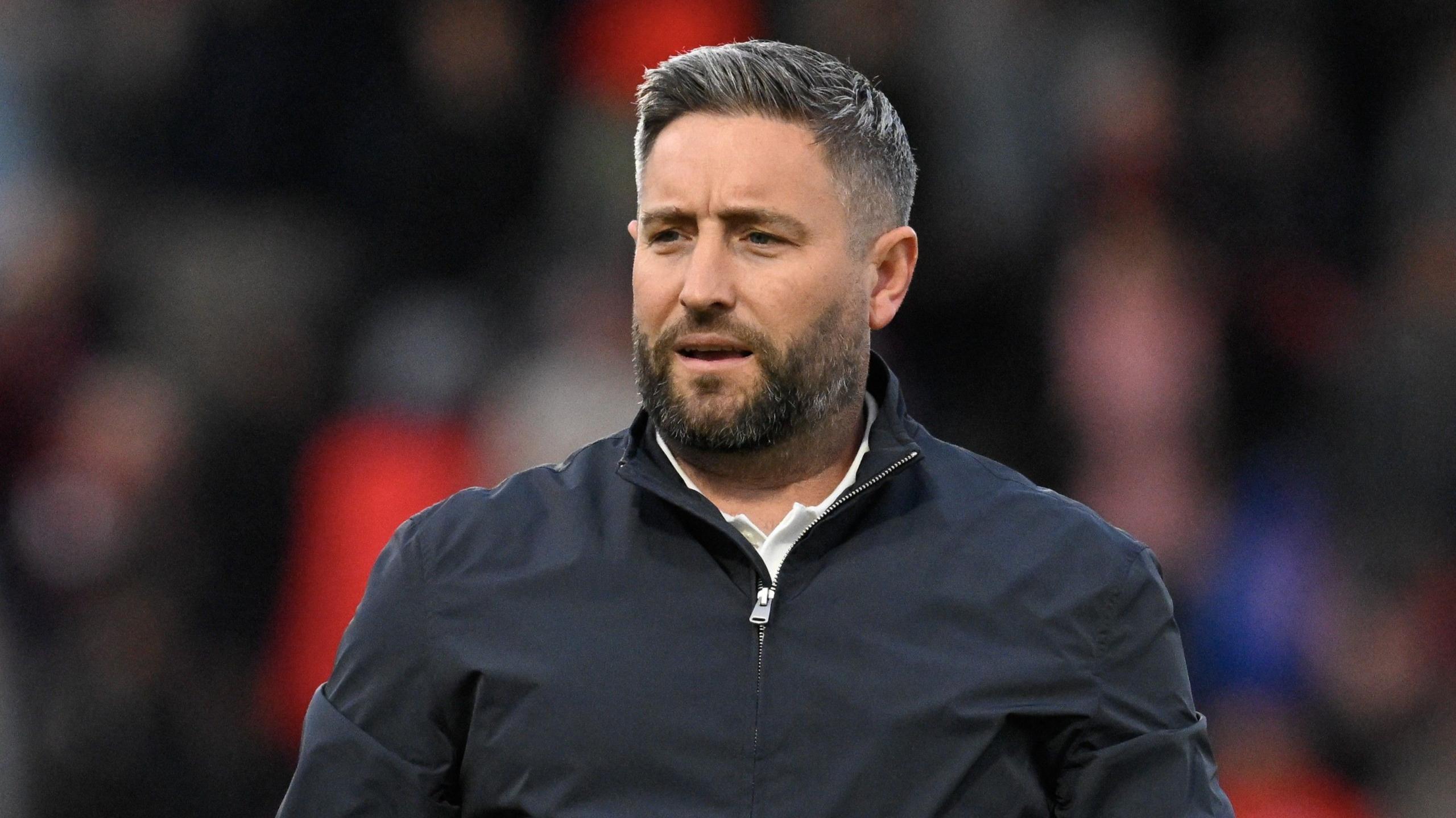 British football manager Lee Johnson during a Belgian second division match. Johnson is wearing a plain blue quarter-zip jacket