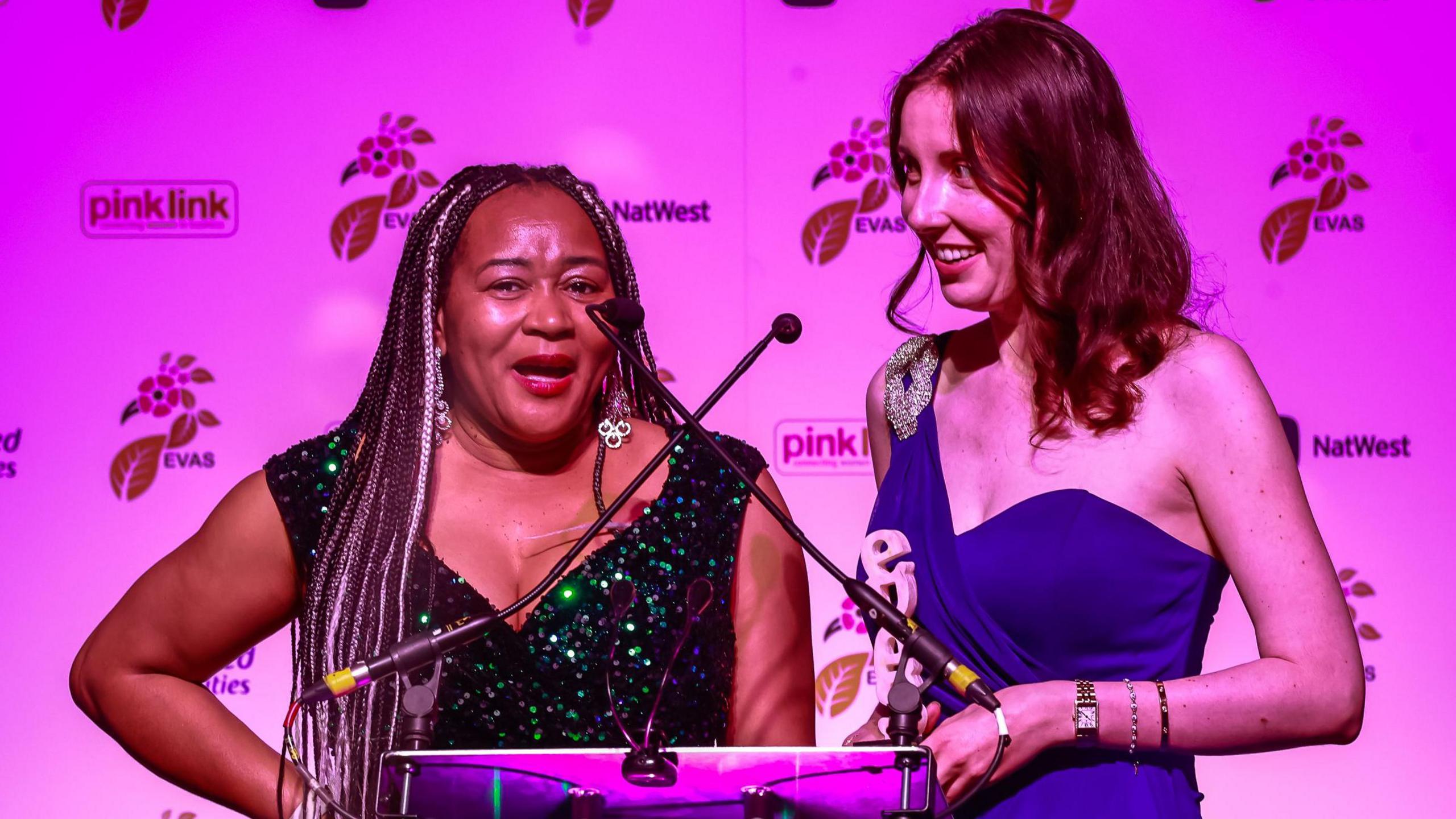 Shalom LLoyd accepting her award with Hannah White, Shalom is a black sequined dress and Hannah a blue gown on one shoulder.