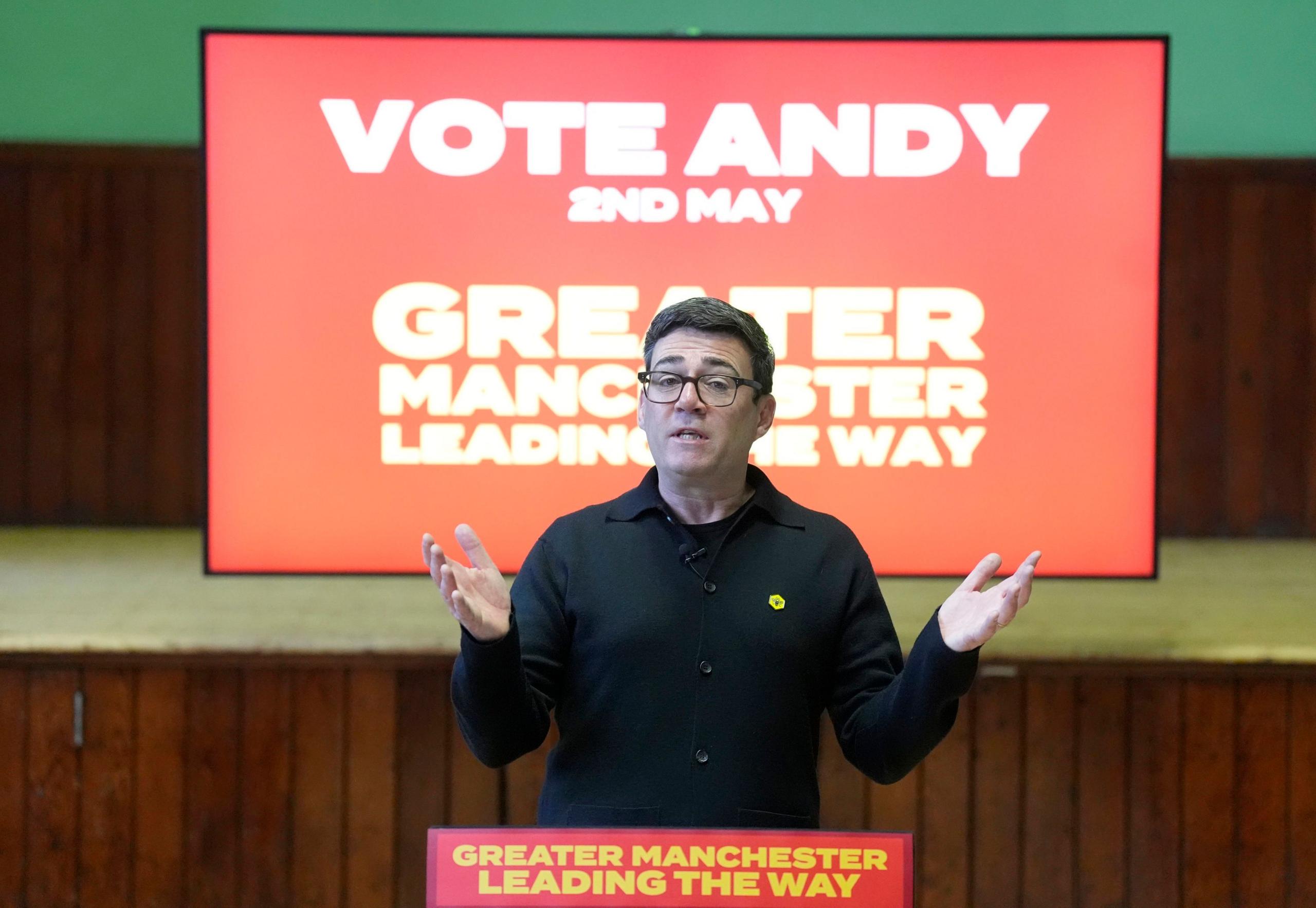 Andy Burham during a campaign speech. He is standing in front of a screen which reads 'Vote Andy'. He is speaking at a lectern with a sign that reads: 'Greater Manchester leading the way' 