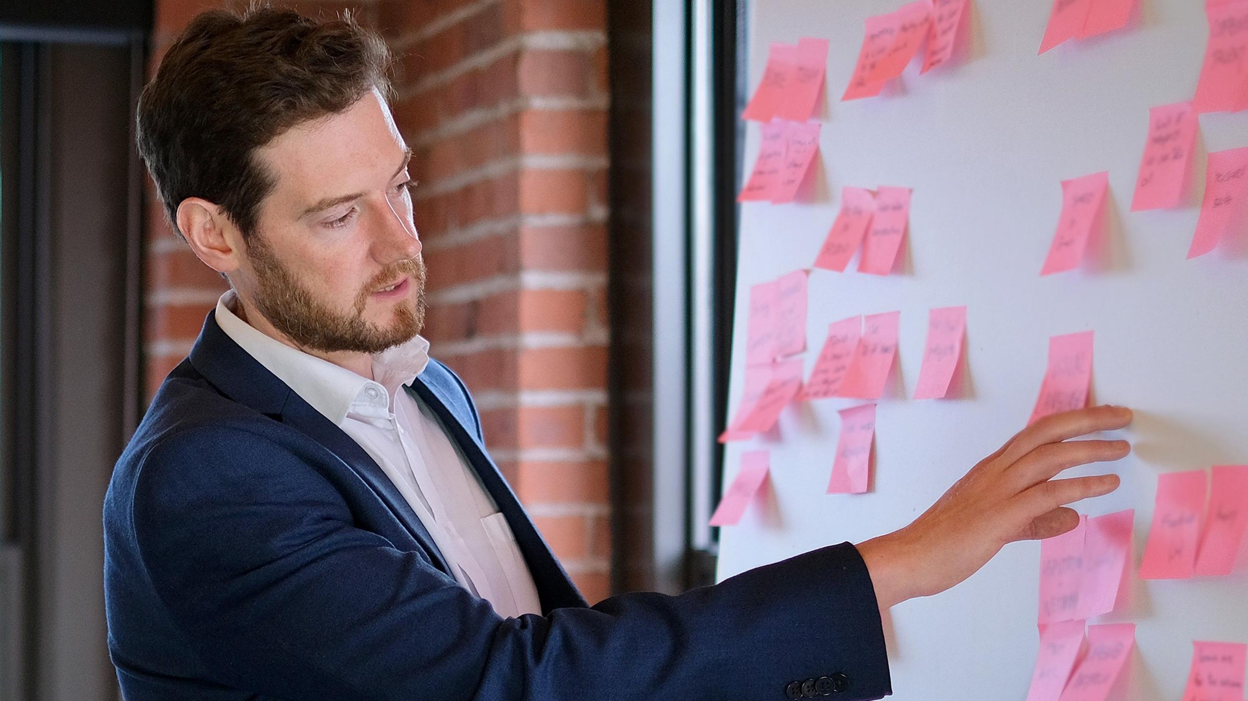 Charlie Paterson looks a white board covered in pink notes