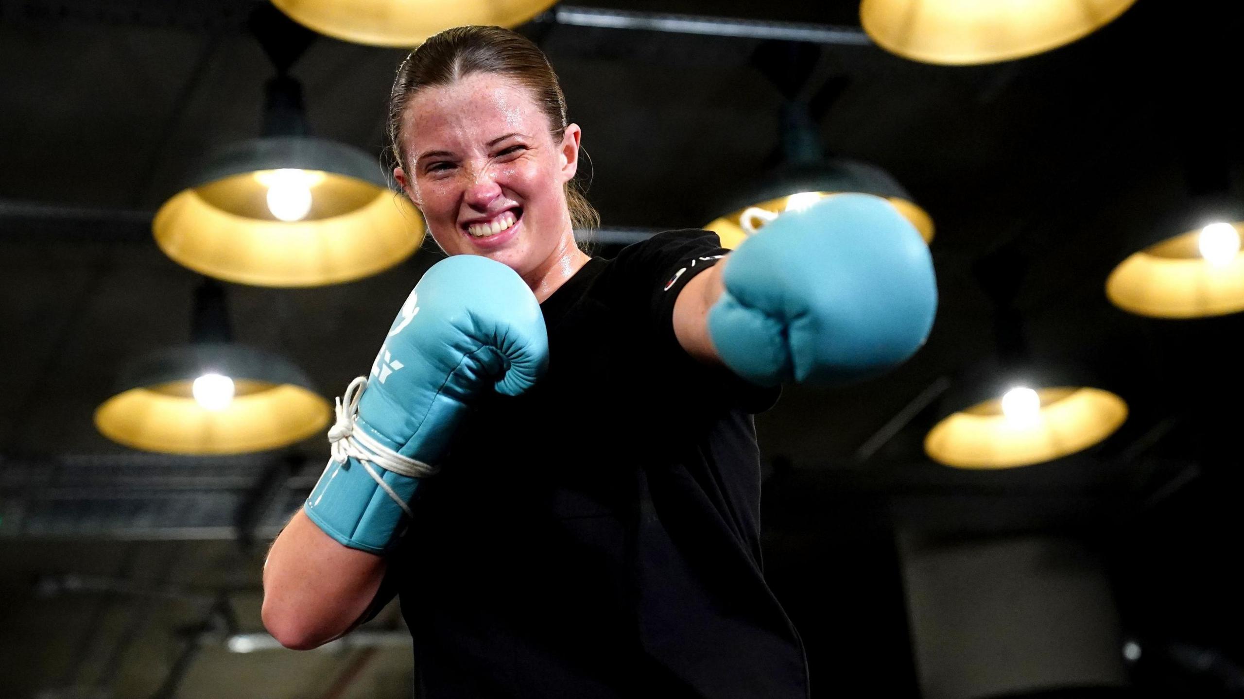 Fran Hennessy, known as the Billion Dollar Baby, punches the air wearing sky blue gloves with a smile on her face.