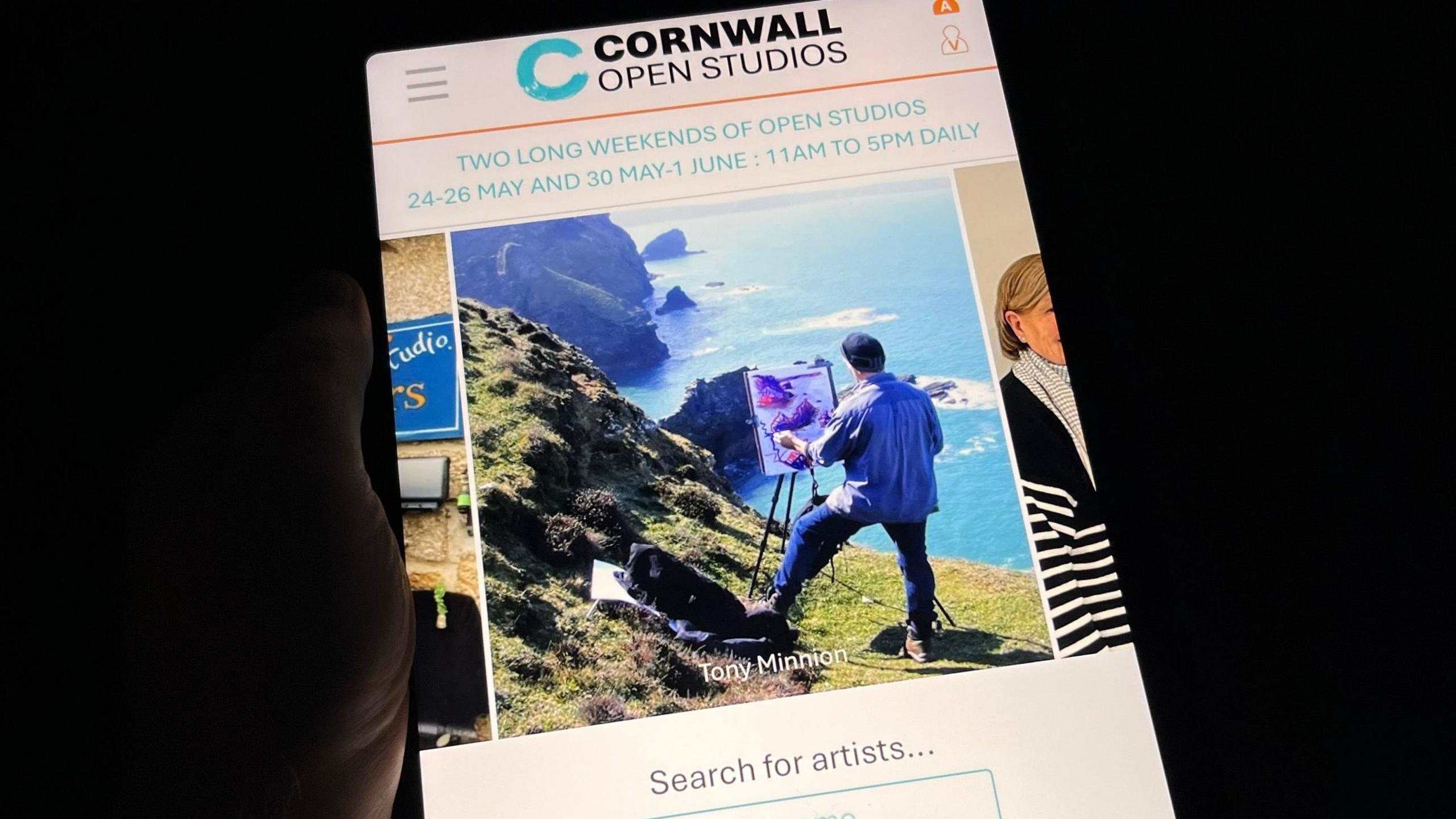 A website on an tablet computer. The logo is a baby blue C with a weathered effect and Cornwall Open Studios in black. The site has a carousel of images, with a photo of artist Tony Minnion painting a landscape on top of a cliff.