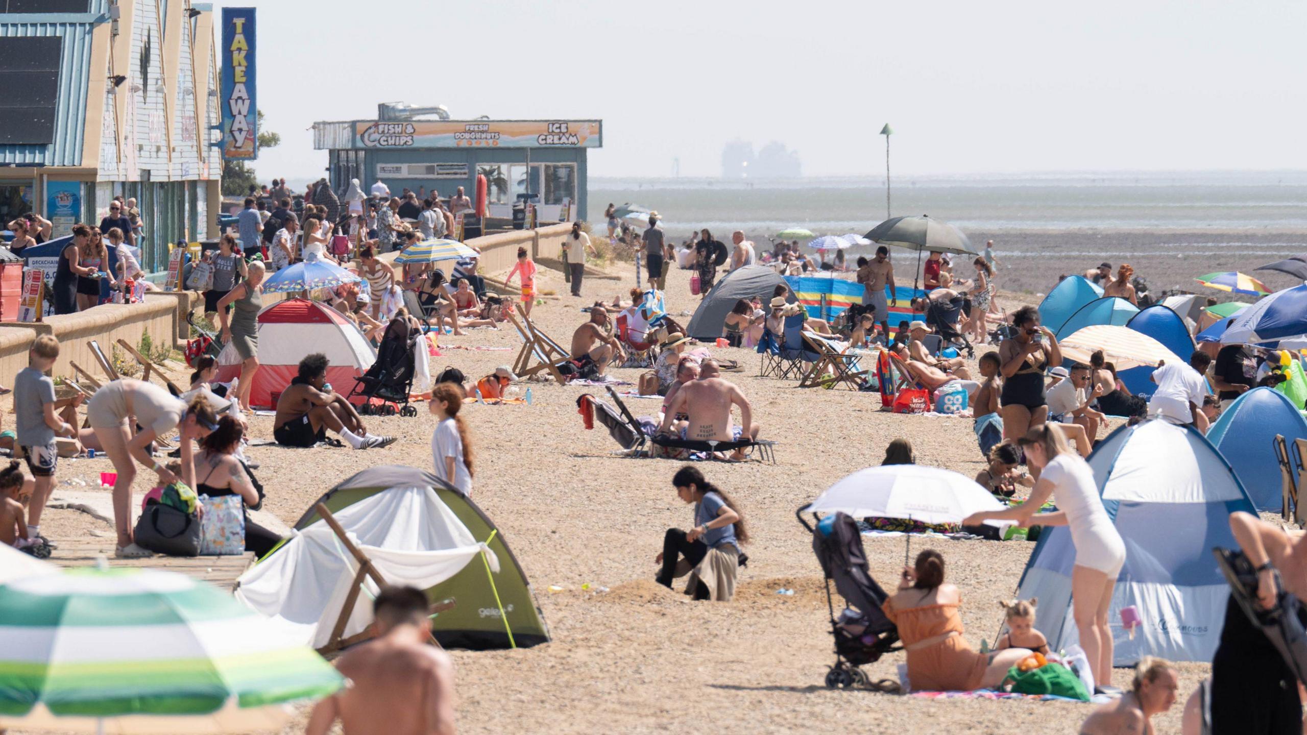 A crowded beach with parasols and beach tents, and the sea in the distance