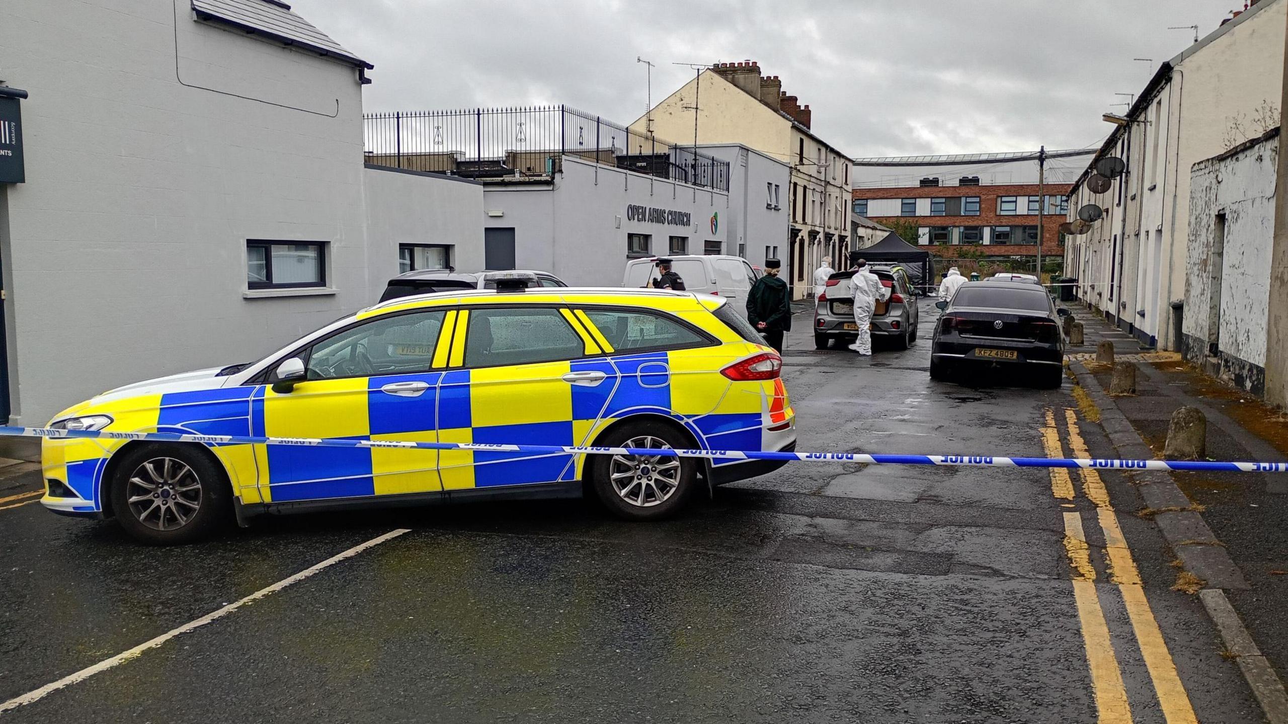 Harford Street in Portadown. In the foreground is a police car, with blue and white tape blocking off the street. Police officers in forensic suits are on the street. 