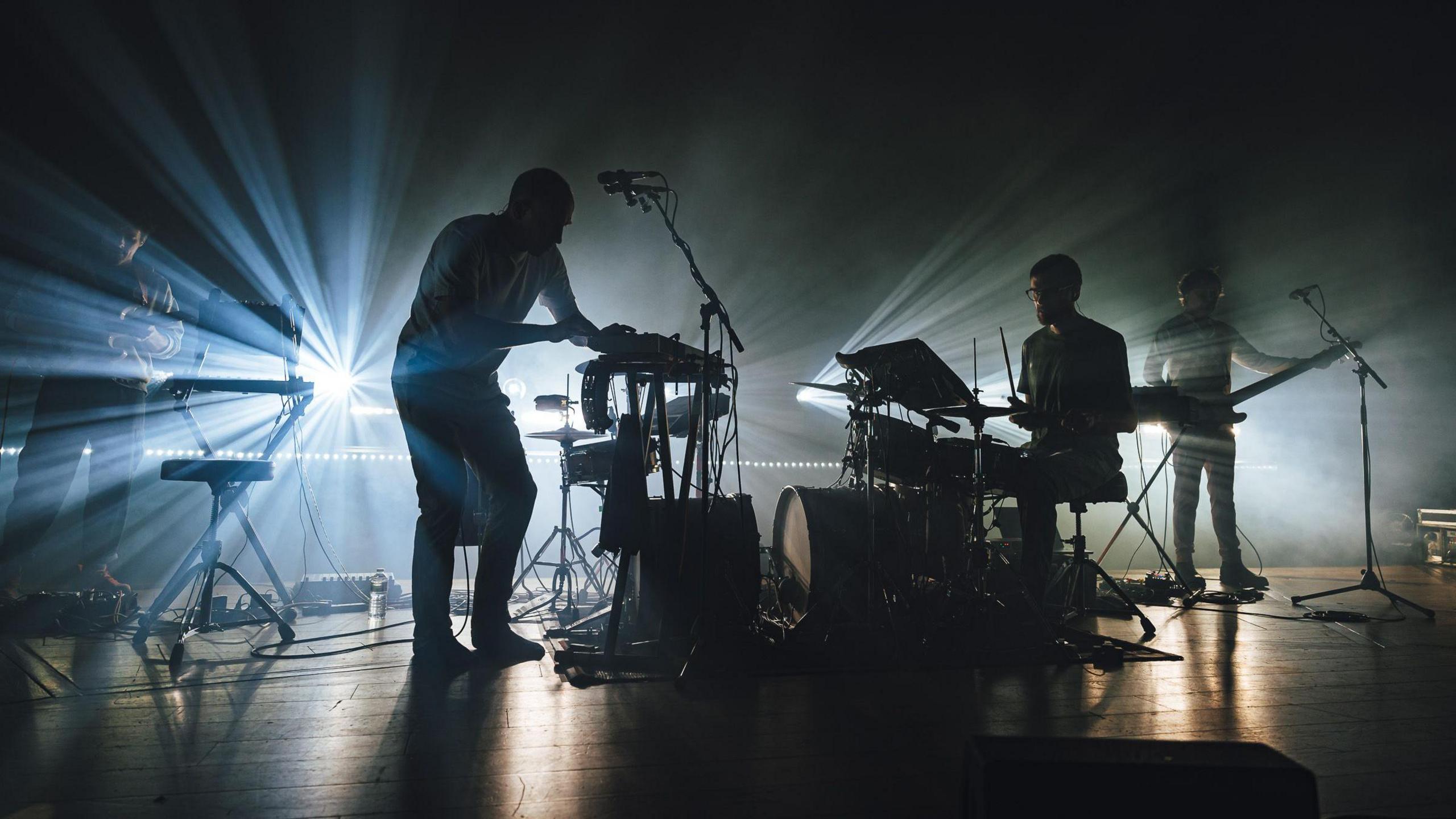 Members of the band Caribou are silhoutted by spotlights behind them as they perform on stage at Bristol Beacon