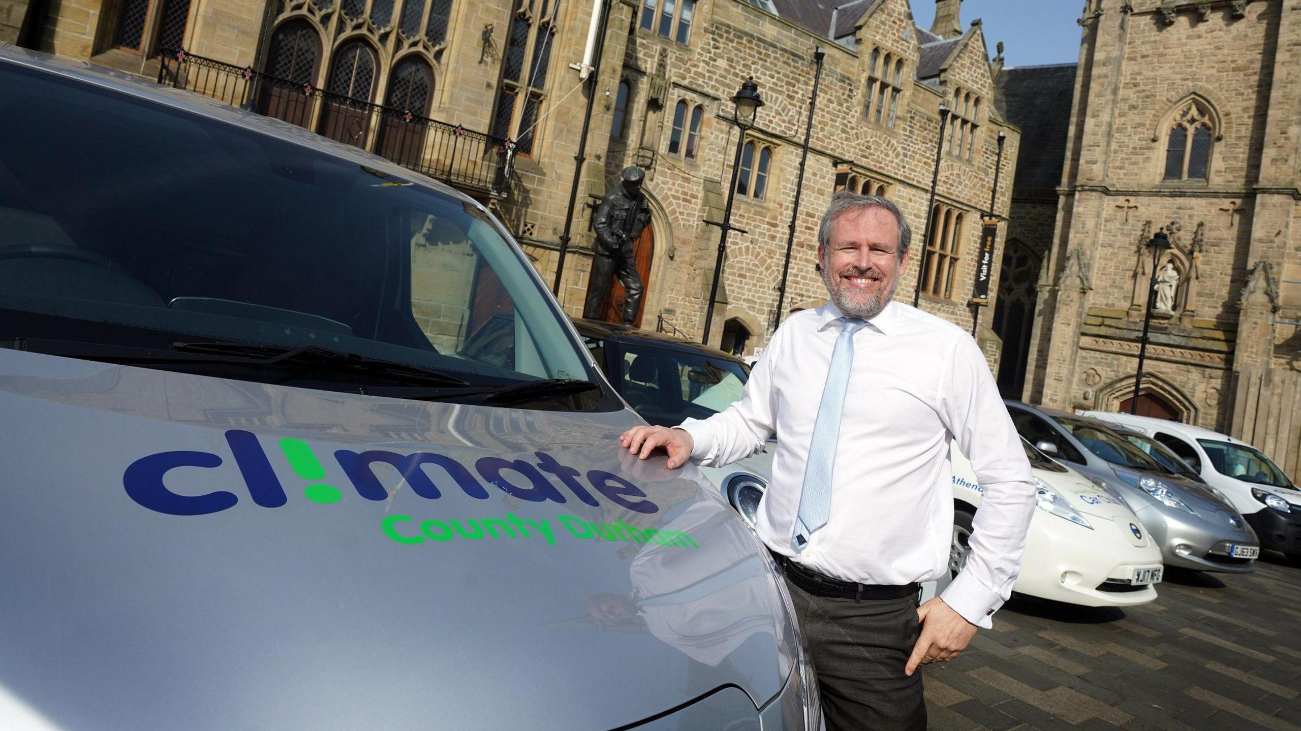 Councillor Mark Wilkes. He is wearing a white shirt and light blue tie. He is standing next to a council van which has the words Climate County Durham printed on its bonnet.