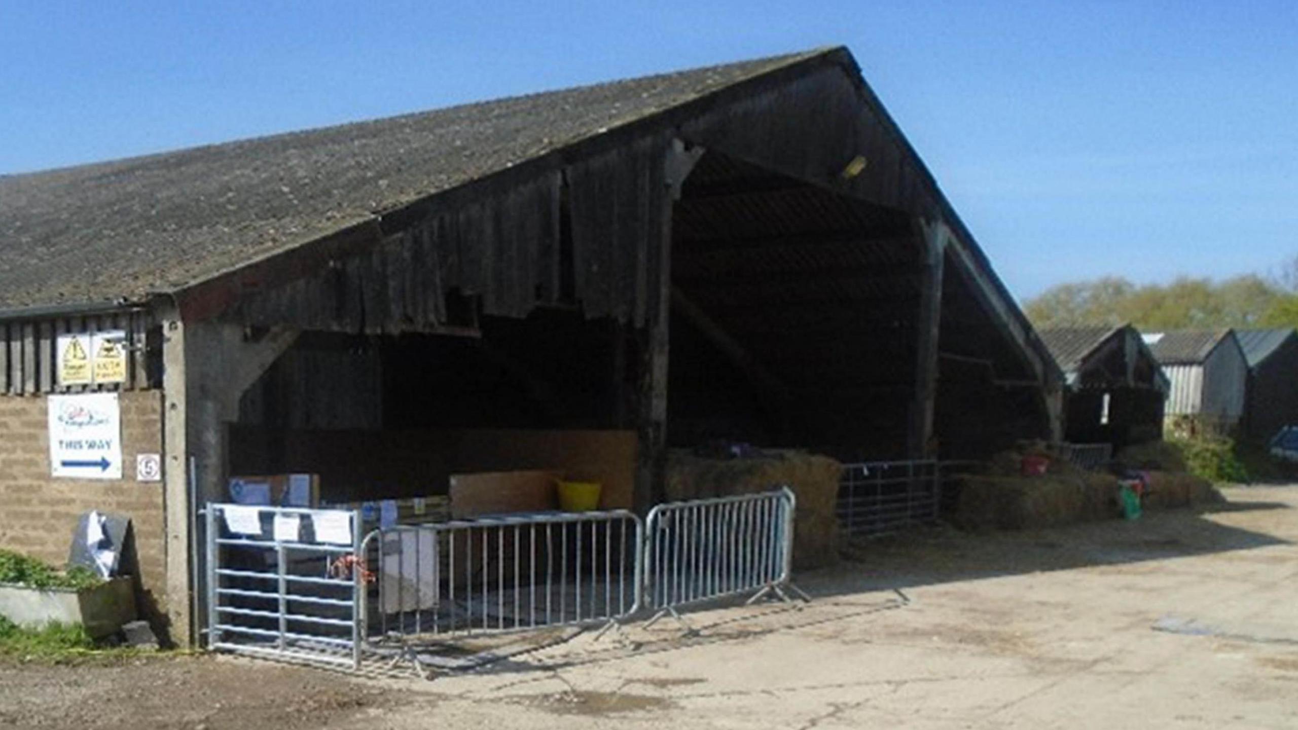 A large brick-built barn at Hazelgrove Farm with metal barriers and bales of hay blocking one open side.
