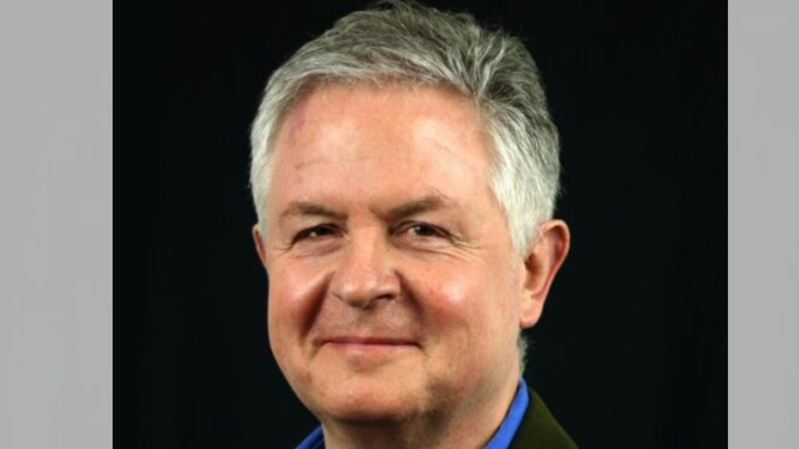 A head shot of a man with short grey hair smiling into the camera