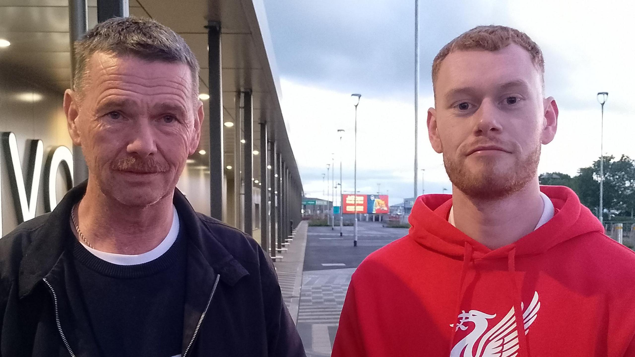 Mr Baxter has short ginger hair and beard, he is wearing a red hoodie and a white top beneath it as he speaks into a black mic held by a reporter.