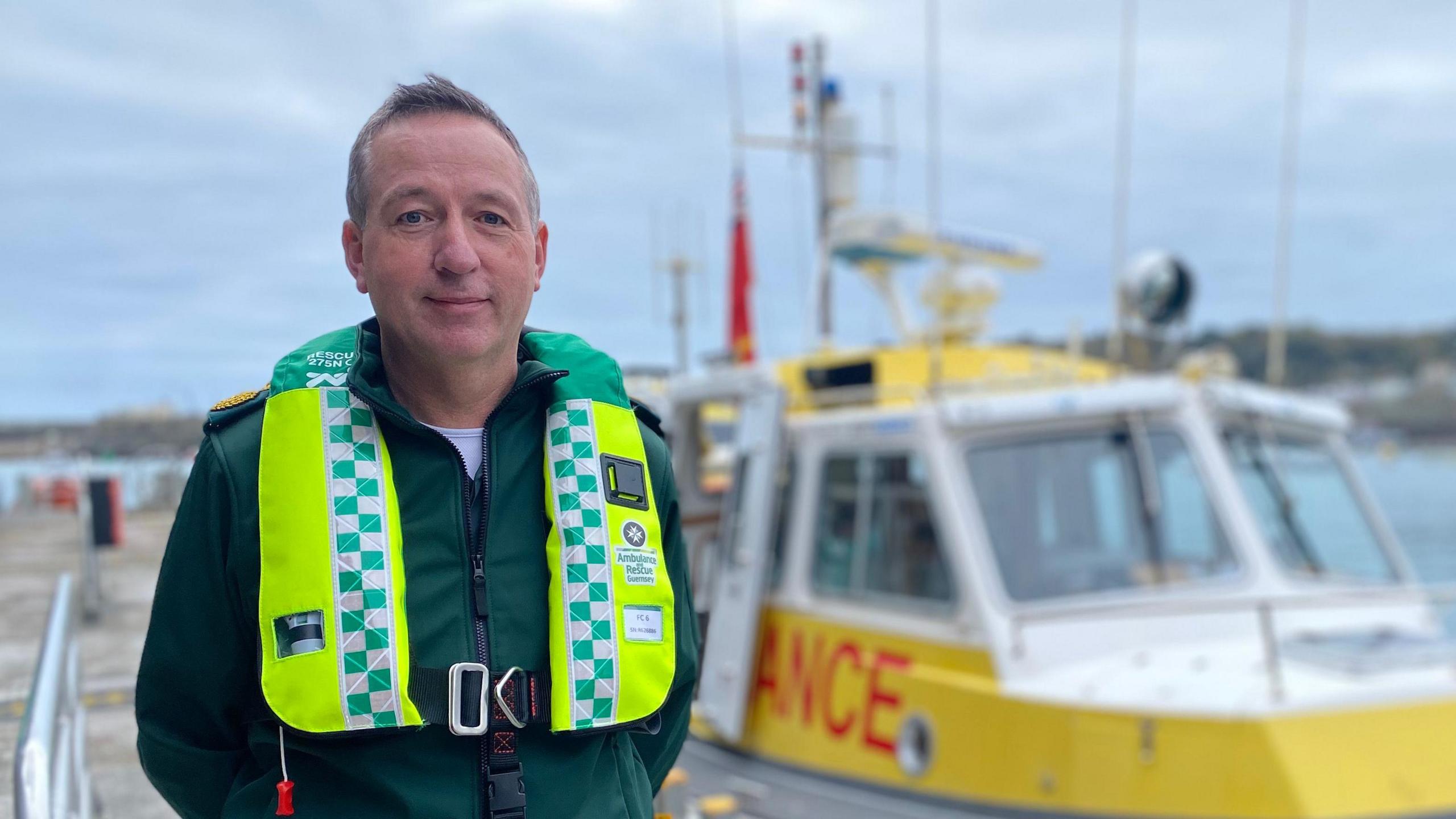 Man in ambulance uniform stood in front of a boat tied up at the inter-island quay in Guernsey's St Peter Port harbour