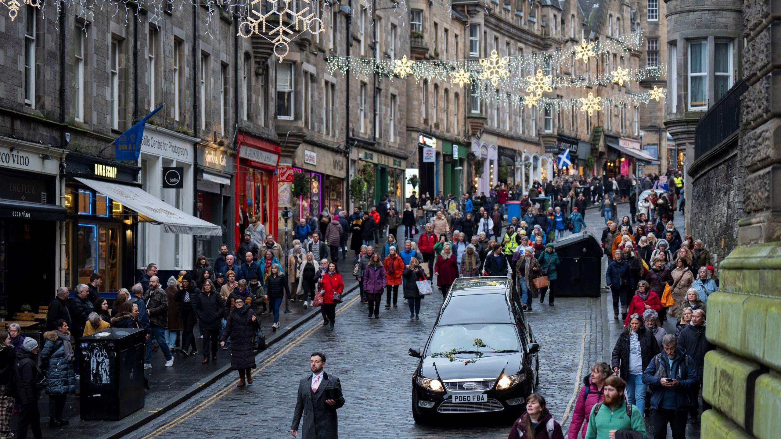 The hearse drives down Cockburn Street, watched by mourners  