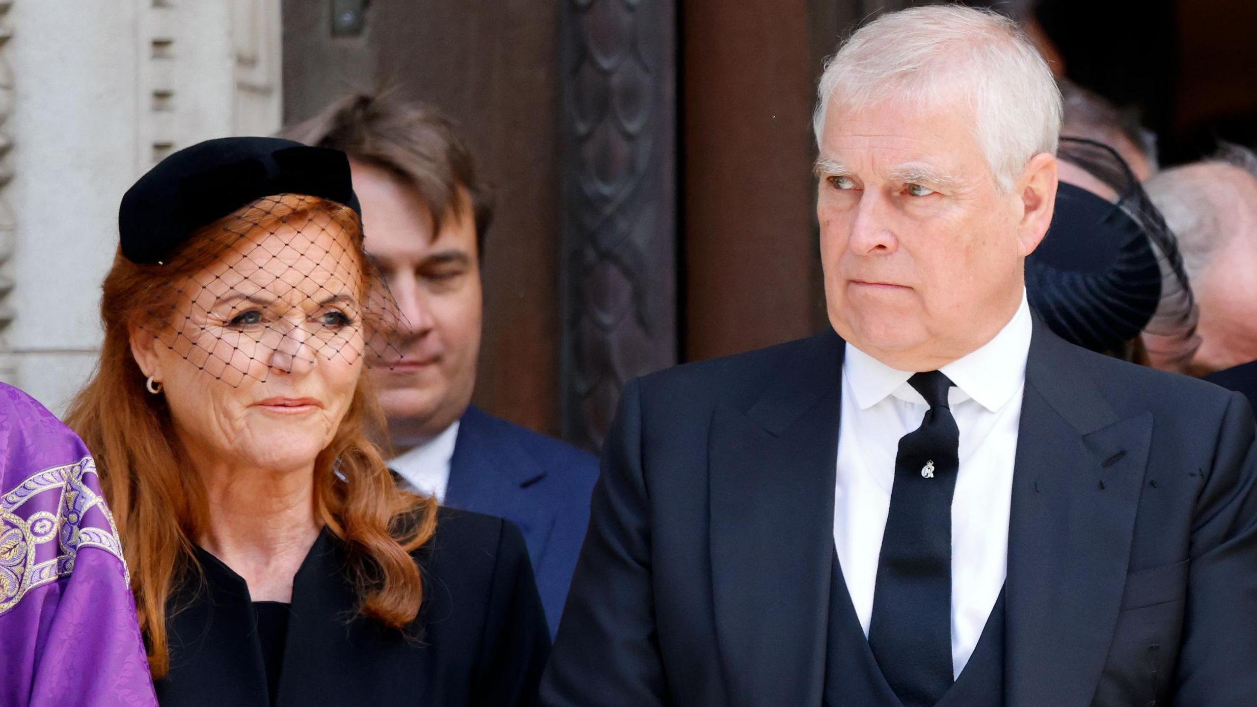 Sarah Ferguson and Andrew attending Duchess of Kent's Requiem Mass service at Westminster Cathedral. She has long ginger hair and is wearing a black dress and hat with a net veil over her face. He is in a black three piece suit with a silver pin on his black tie.