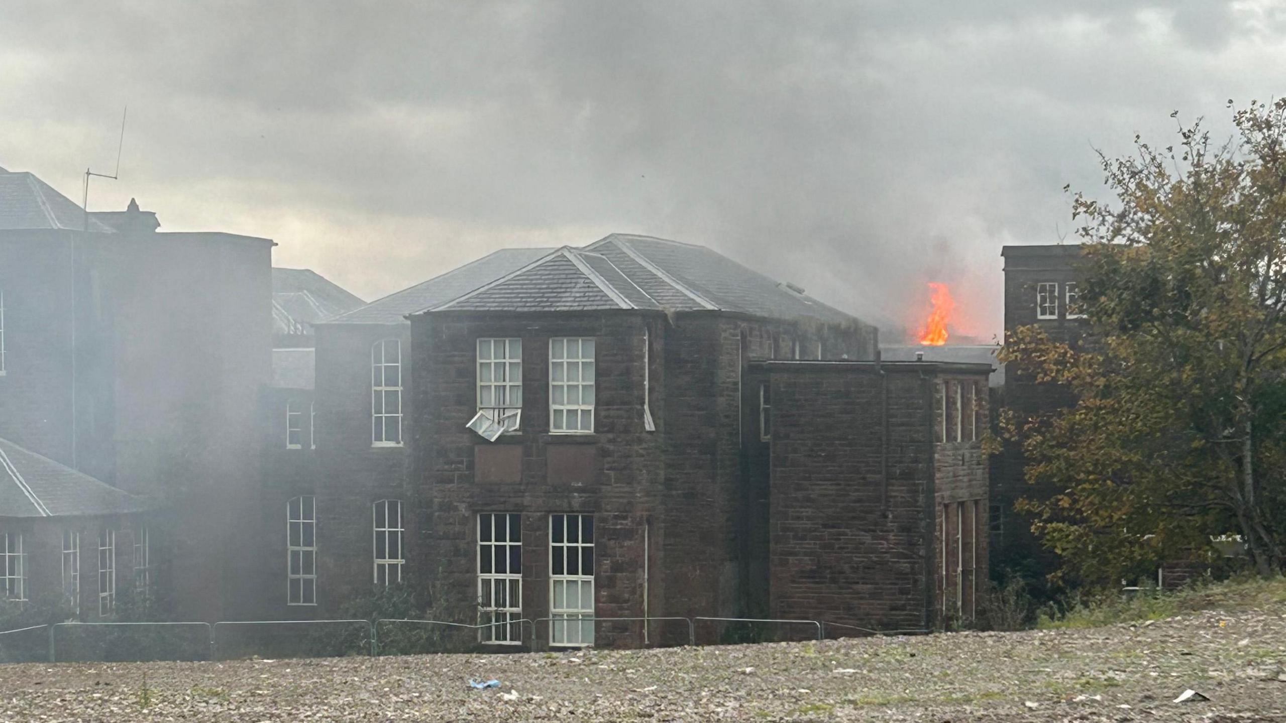 An old sandstone building in Dumfries with flames coming out of the roof and smoke clouding the sky